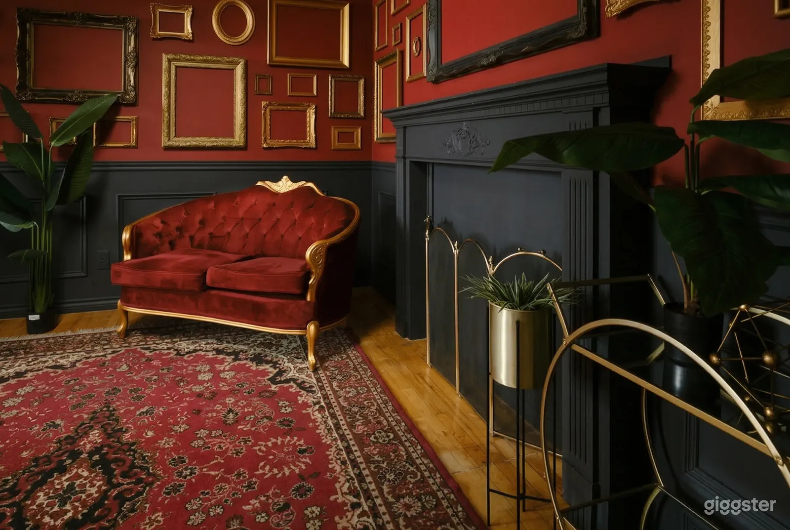 A red velvet vintage couch sits beside a black fireplace in a room with a red carpet on the floor and red walls.