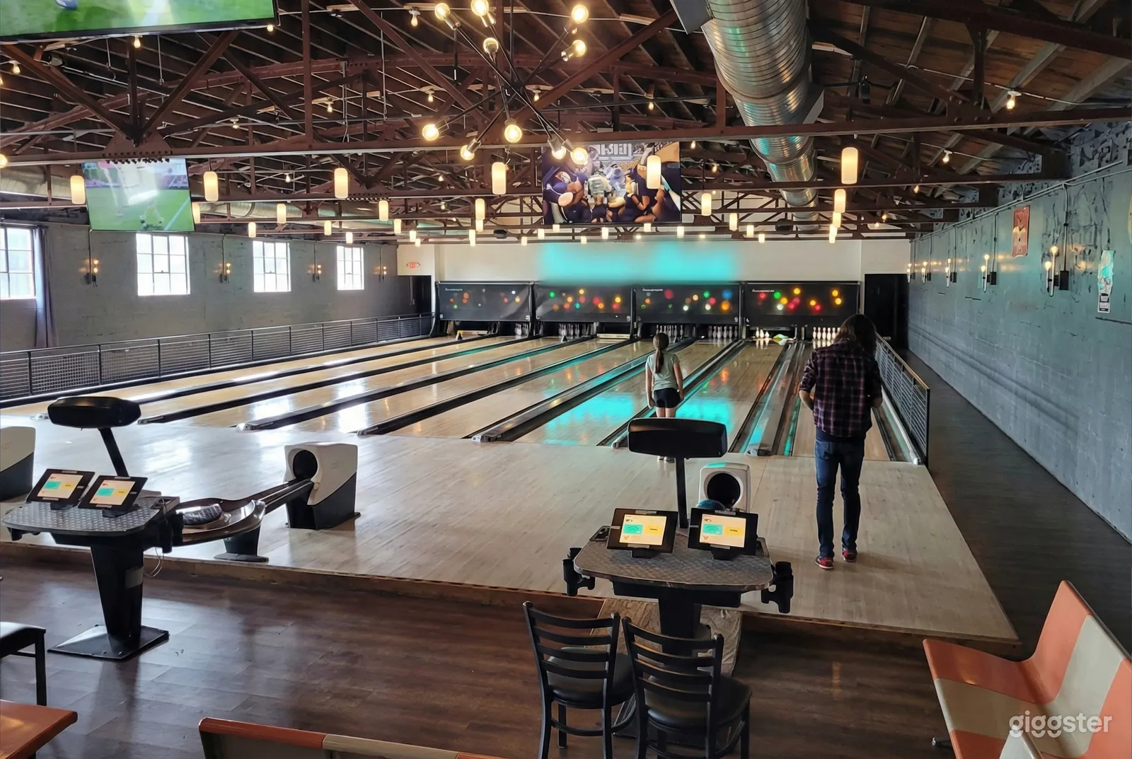 People play in an eight lane bowling alley with a well lit high ceiling.