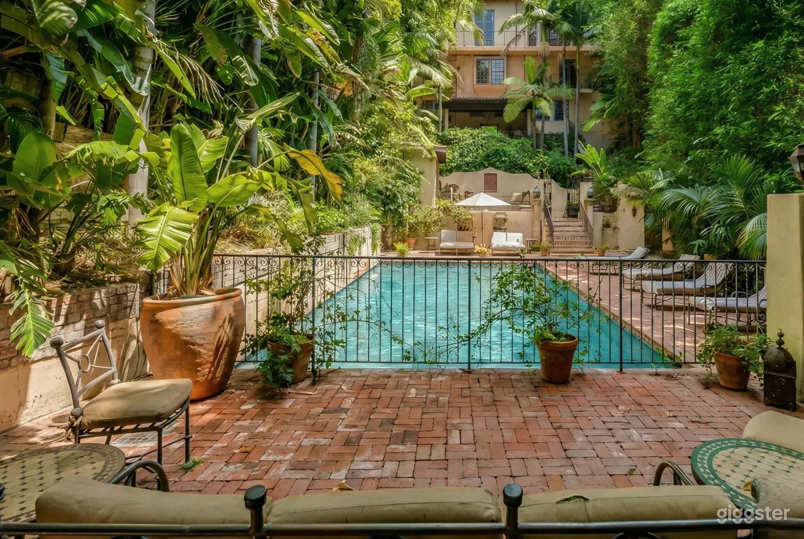 Tree filled stone terrace with a central pool and many loungers at the perimeter.