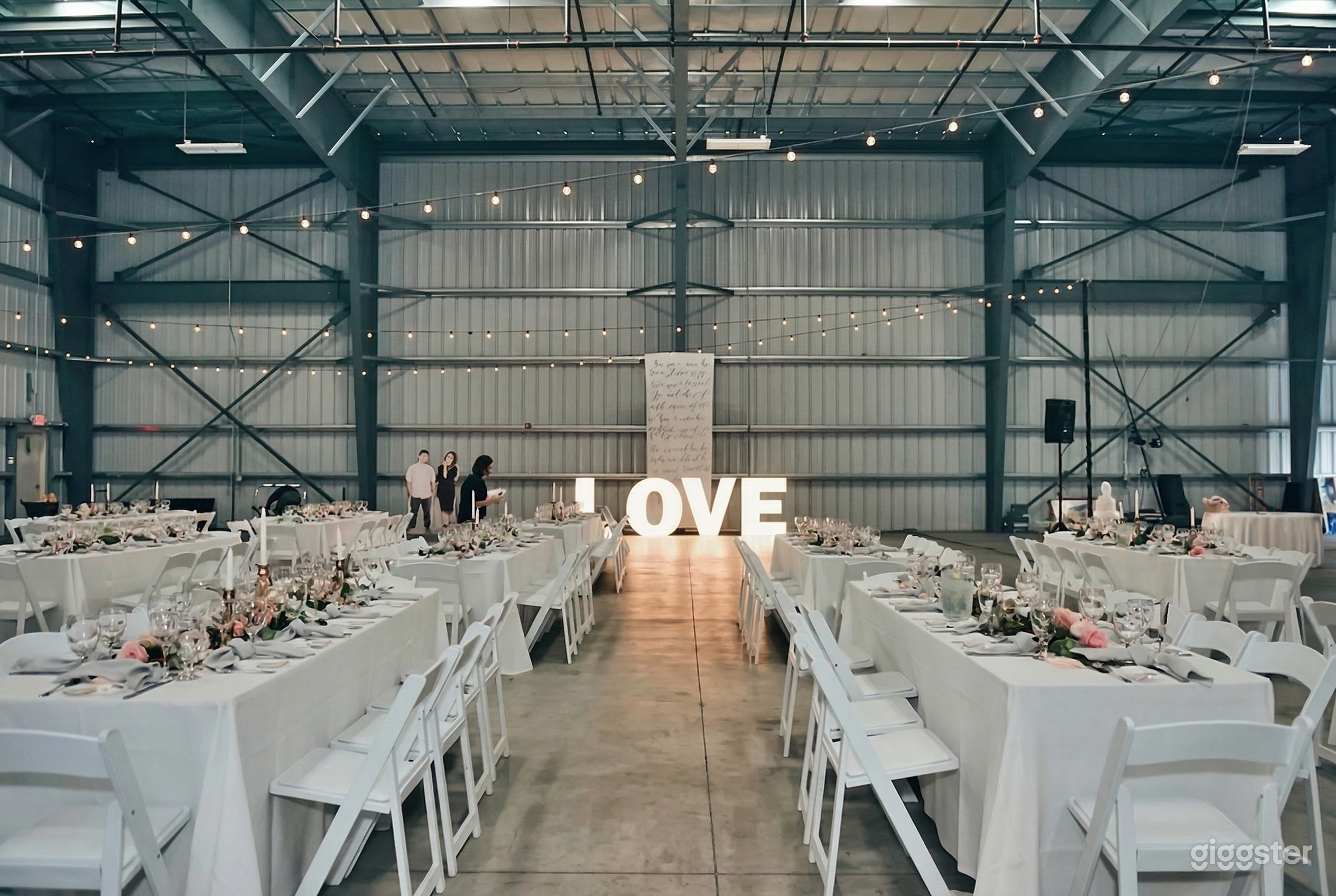 A large warehouse with white steel walls is decorated with banquet tables and chairs, and the tables feature centerpieces.