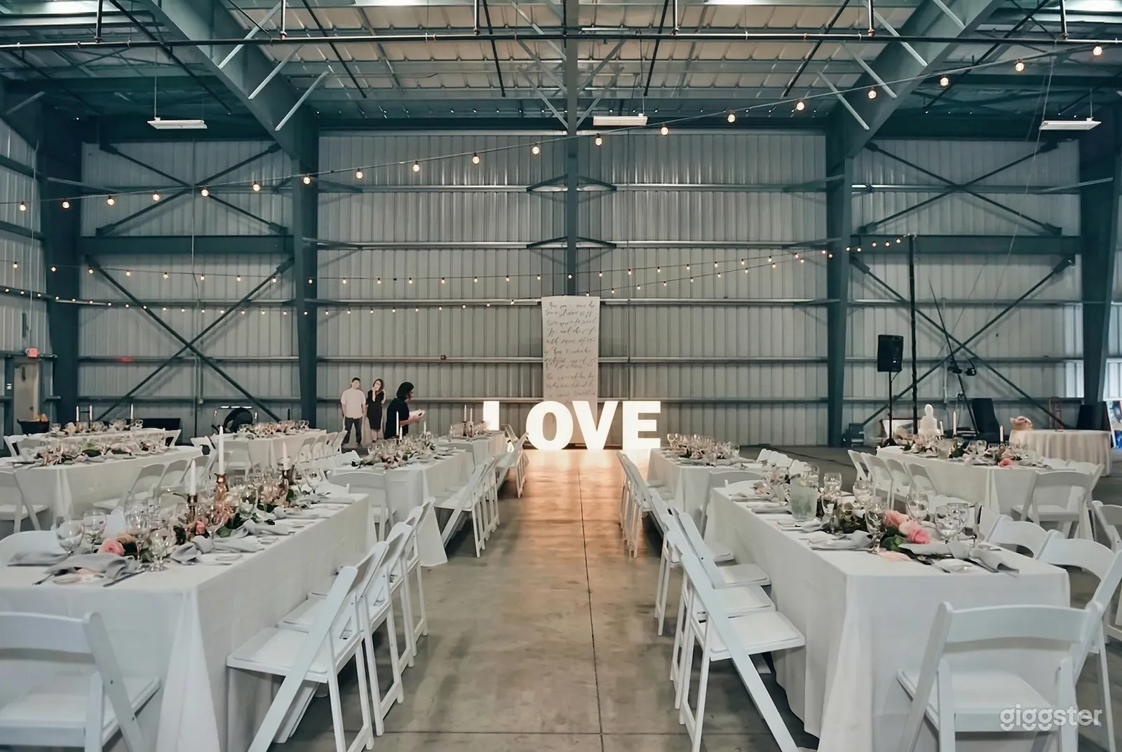 A large warehouse with white steel walls is decorated with banquet tables and chairs, and the tables feature centerpieces.