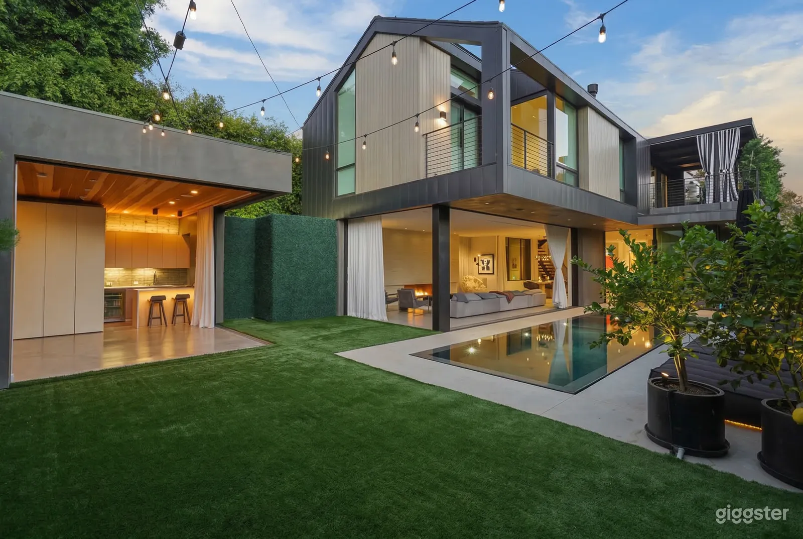 An ultra modern two level home has an open living room downstairs facing a large yard with a stone and glass patio.