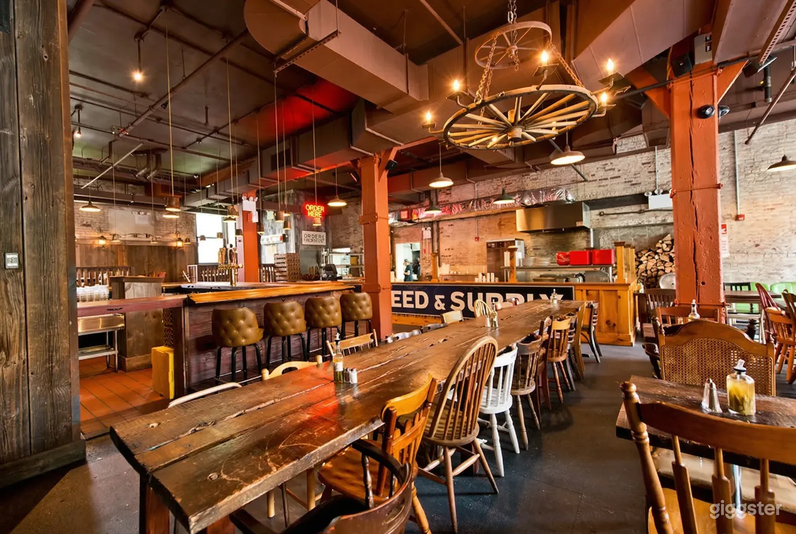 Long wooden tables and a bar are the seating in a casual-style restaurant, decorated with wagon wheel lighting and wooden accents.