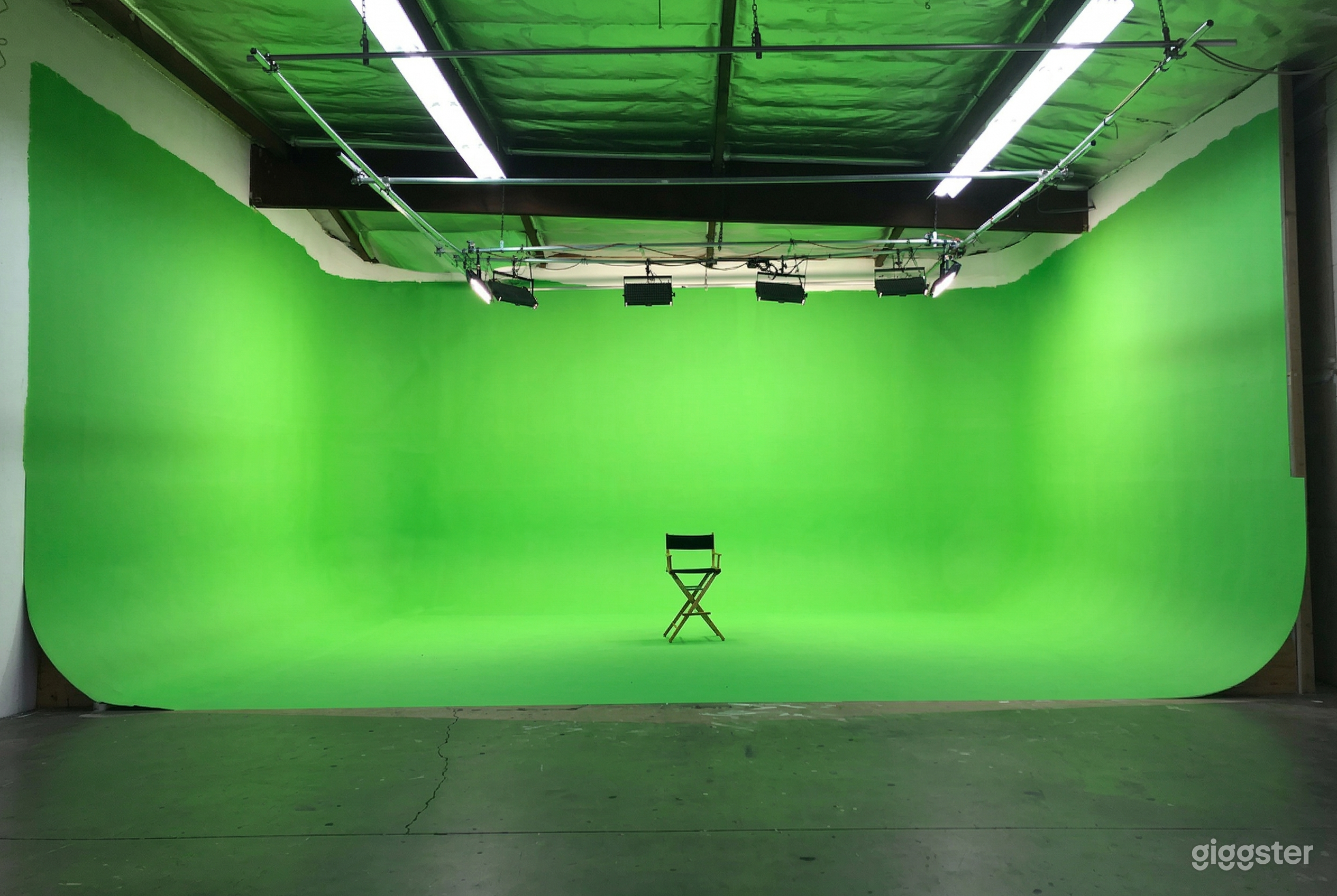 A lone chair under spotlights sits in front of a large room-filling green screen.
