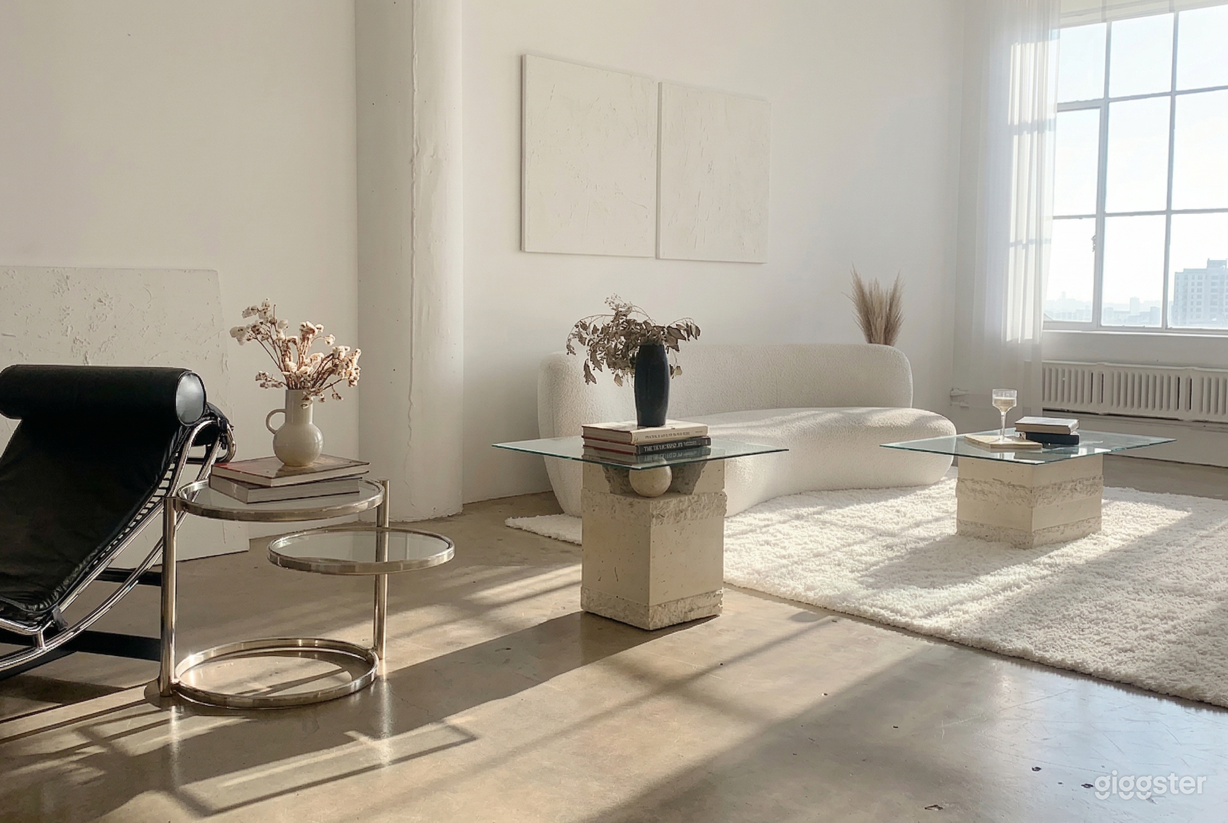 A studio-type space with white couch and carpet, along with occasion tables with glass tops.
