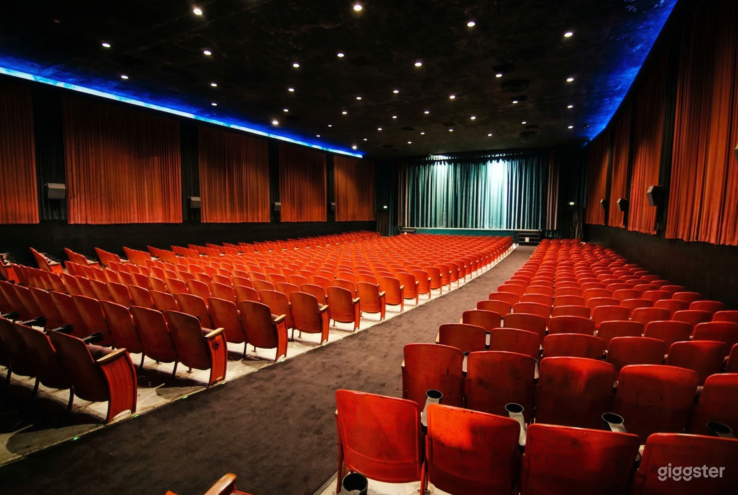 Many rows of red foldup screening chairs face a blue-curtained stage.