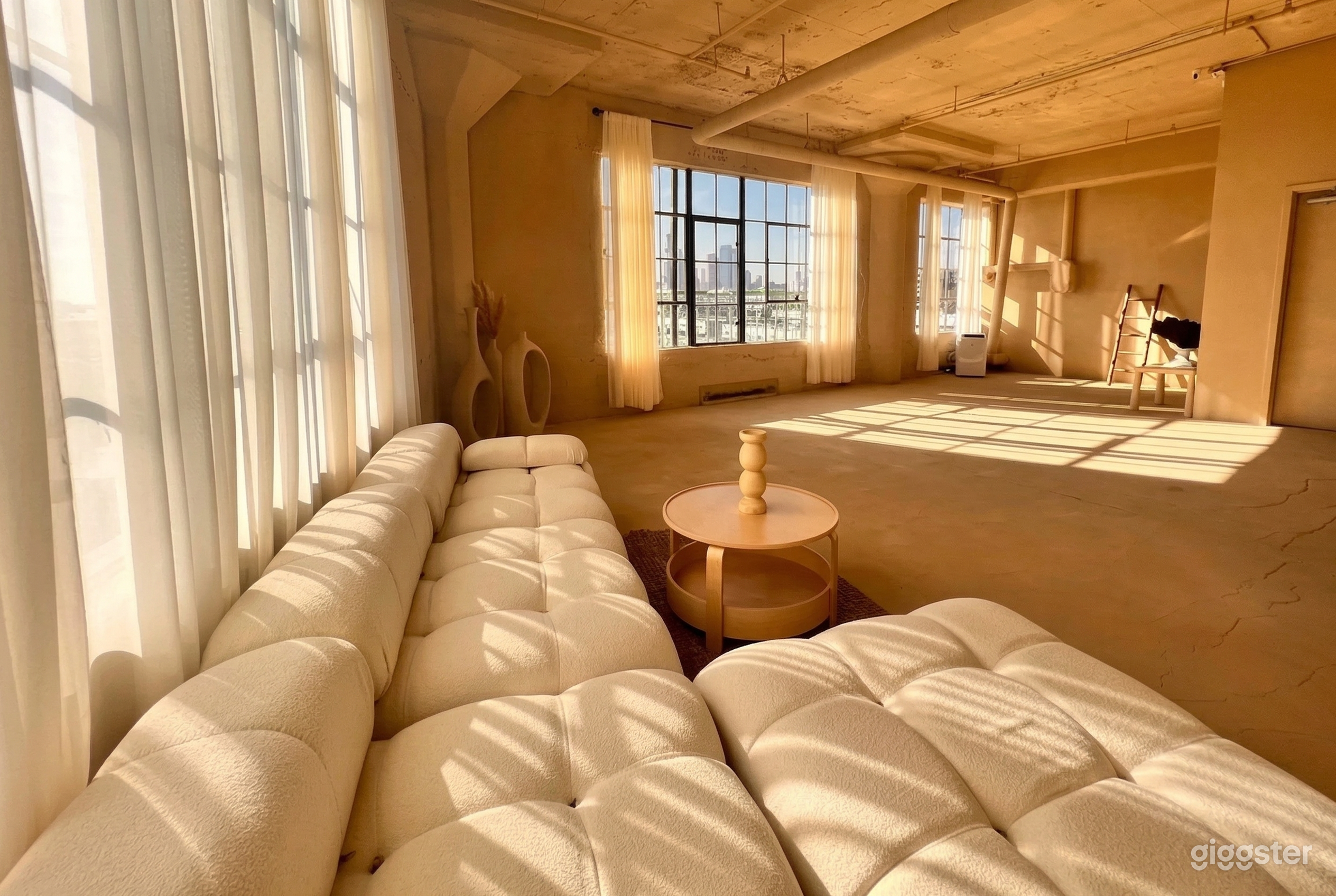 A beige sectional couch is along the wall of a studio type room with big windows and a textured floor.