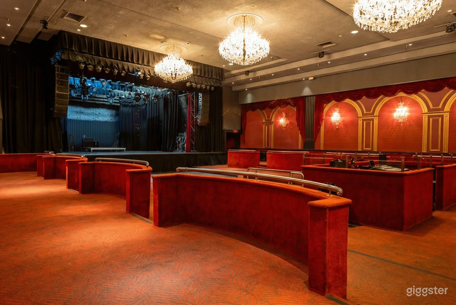 Ballroom style venue in soft red wood colors with a sound board and stage complete with lighting equipment.