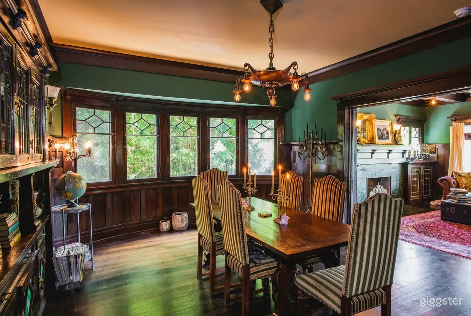 A traditionally decorated dining room with long table and cushioned chairs has a circular wall at the end with diamond paned windows.