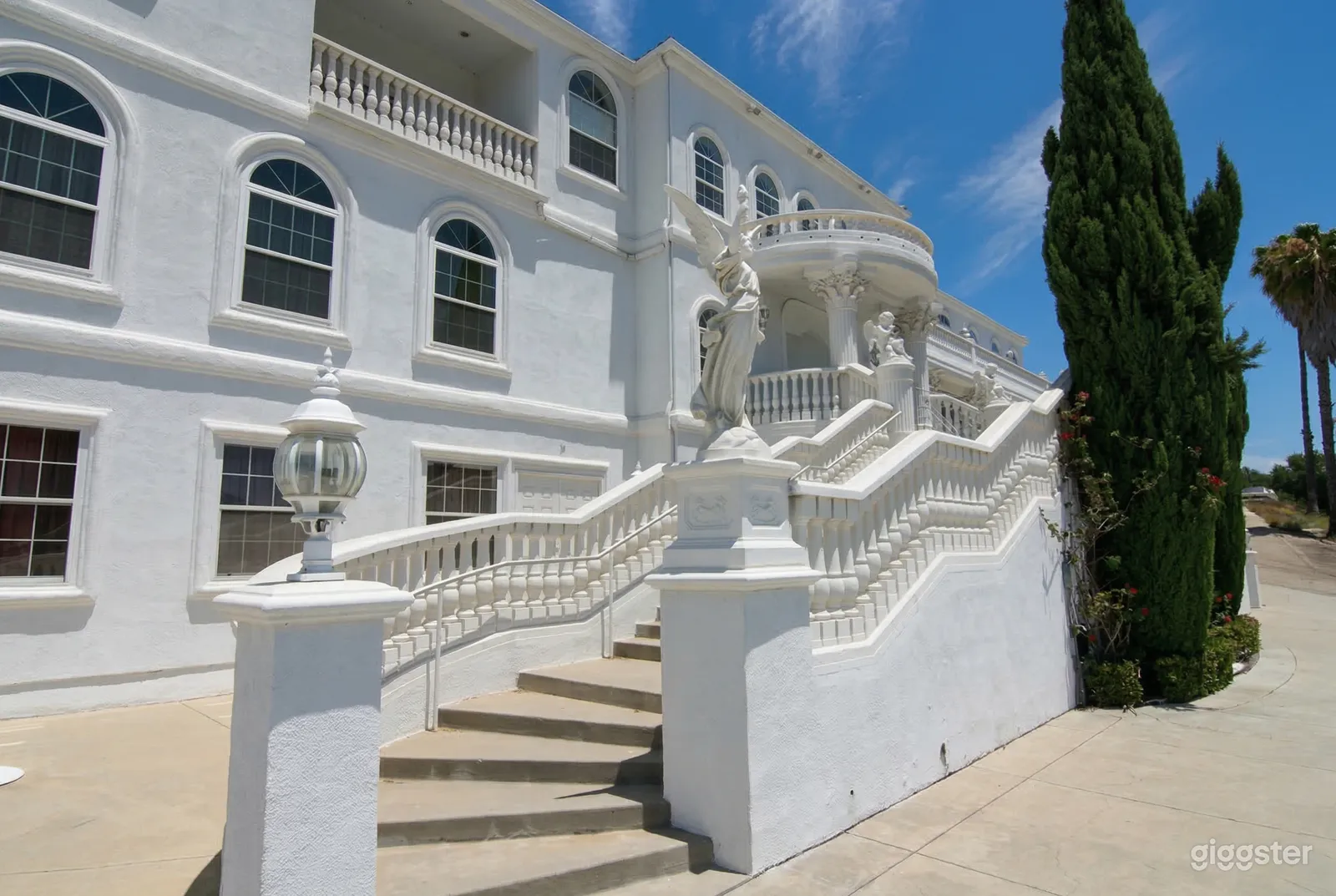 A massive white painted cement building with an ornate stairway decorated with winged statues and columns.