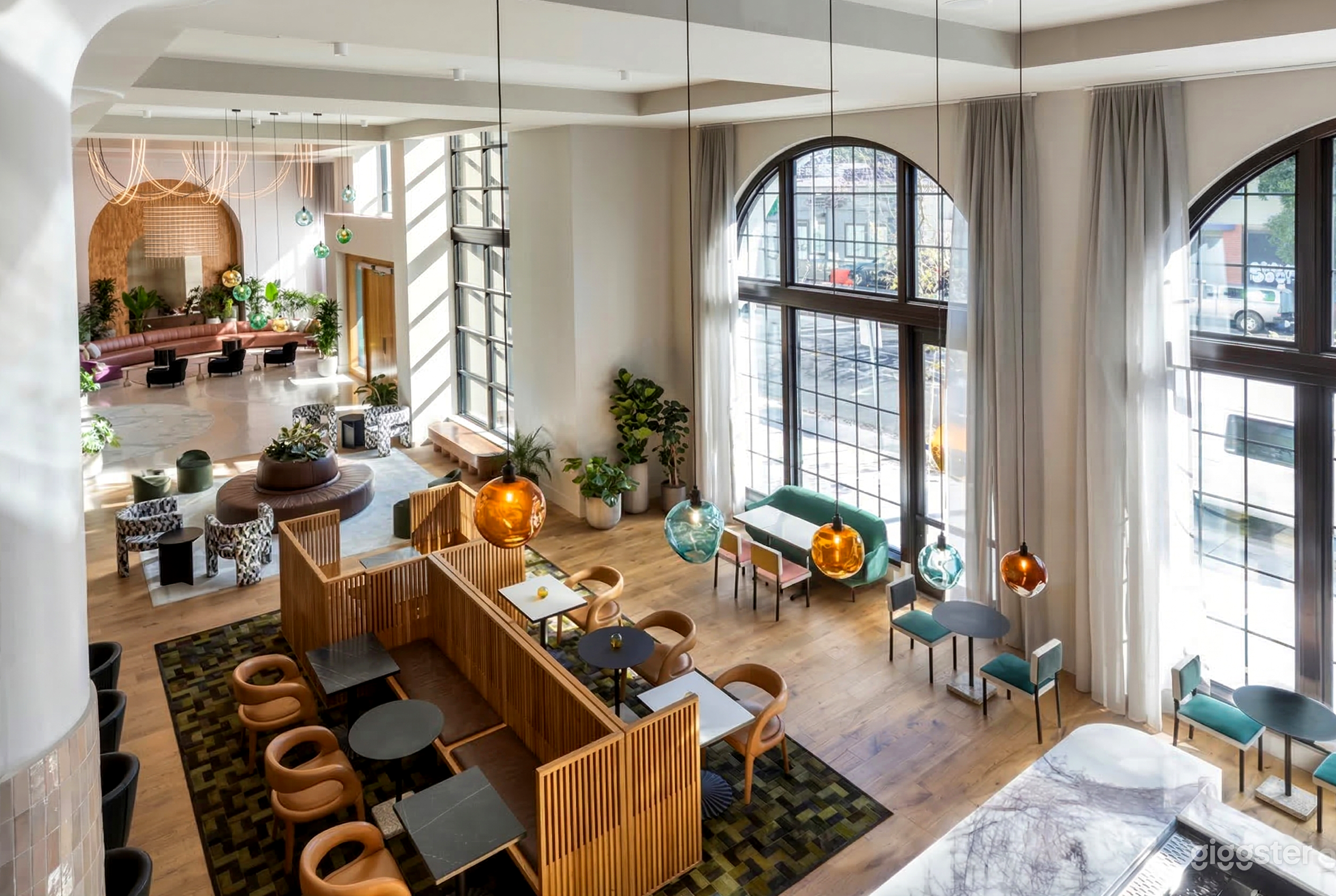 A hotel dining area with distinct seating areas of turquoise, black and wood, and more sit in front of floor to ceiling windows.