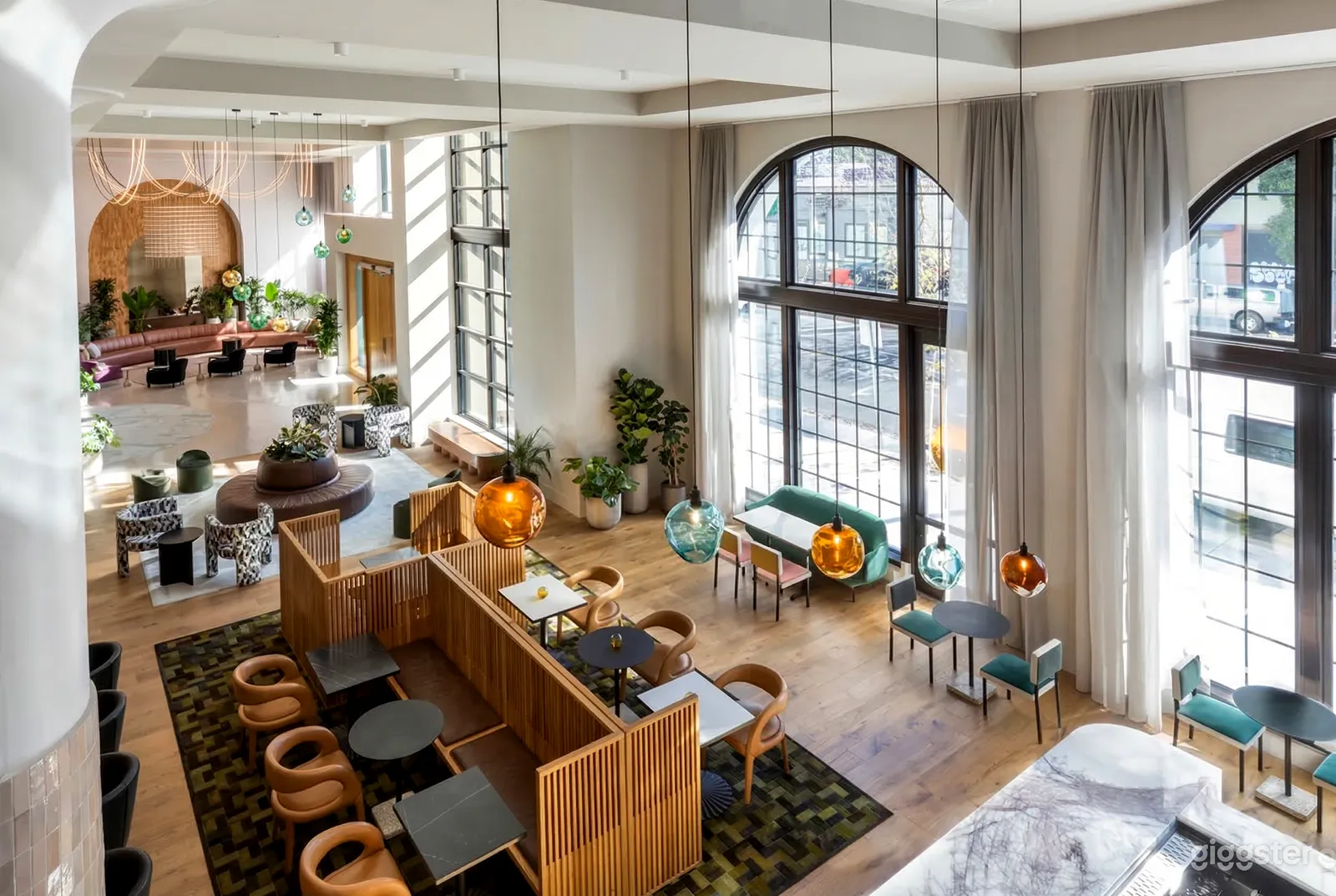 A hotel dining area with distinct seating areas of turquoise, black and wood, and more sit in front of floor to ceiling windows.