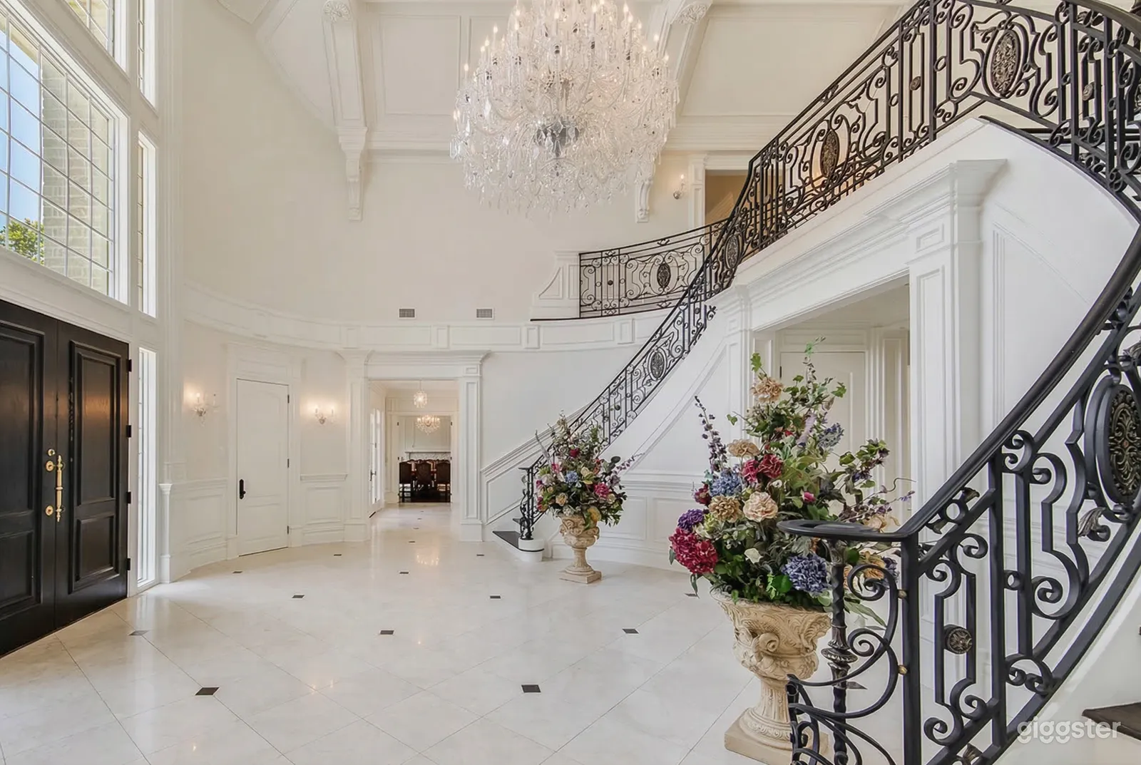 Colorful flower displays frame an arched entrance with stairways on either side decorated with wrought iron railings. 