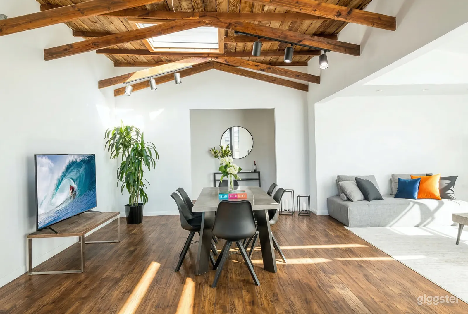 A modern style room with a central dining table, grey couches and wood beamed ceiling.