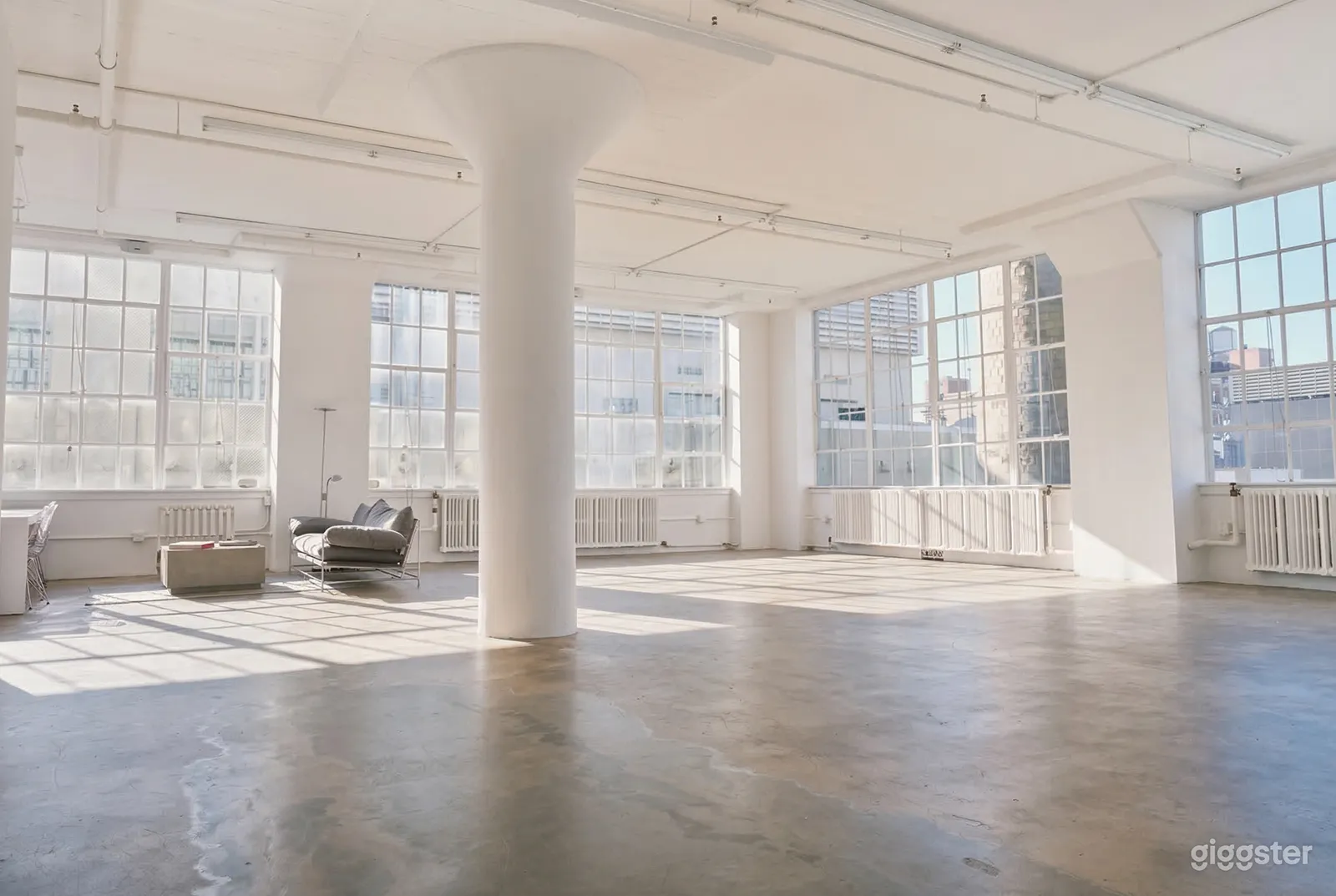 A large sunny white event room has big squared windows and circular columns.