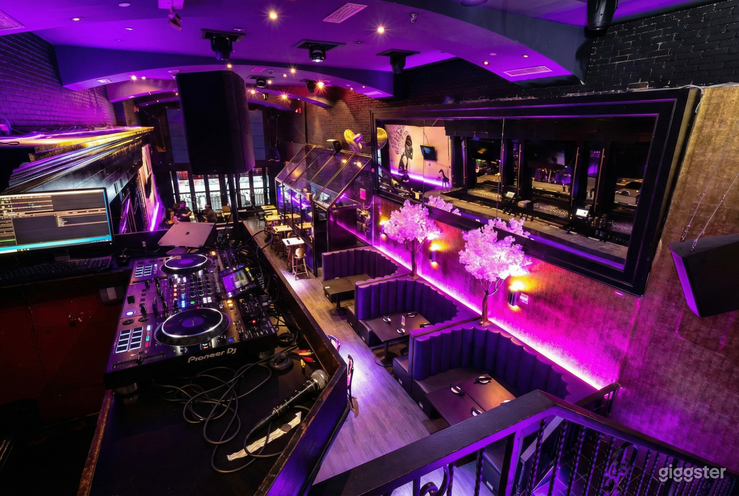 Purple lit club venue with a DJ setup and multiple booths and tables.