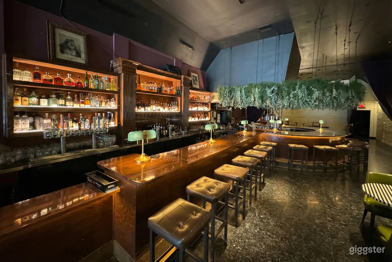 Stools line a polished wooden bar with cocktail mixers lined on the shelves behind.