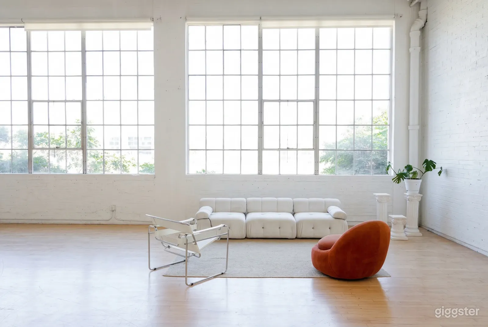 A white industrial style room has minimal seating, a large open space, and expansive paned windows.