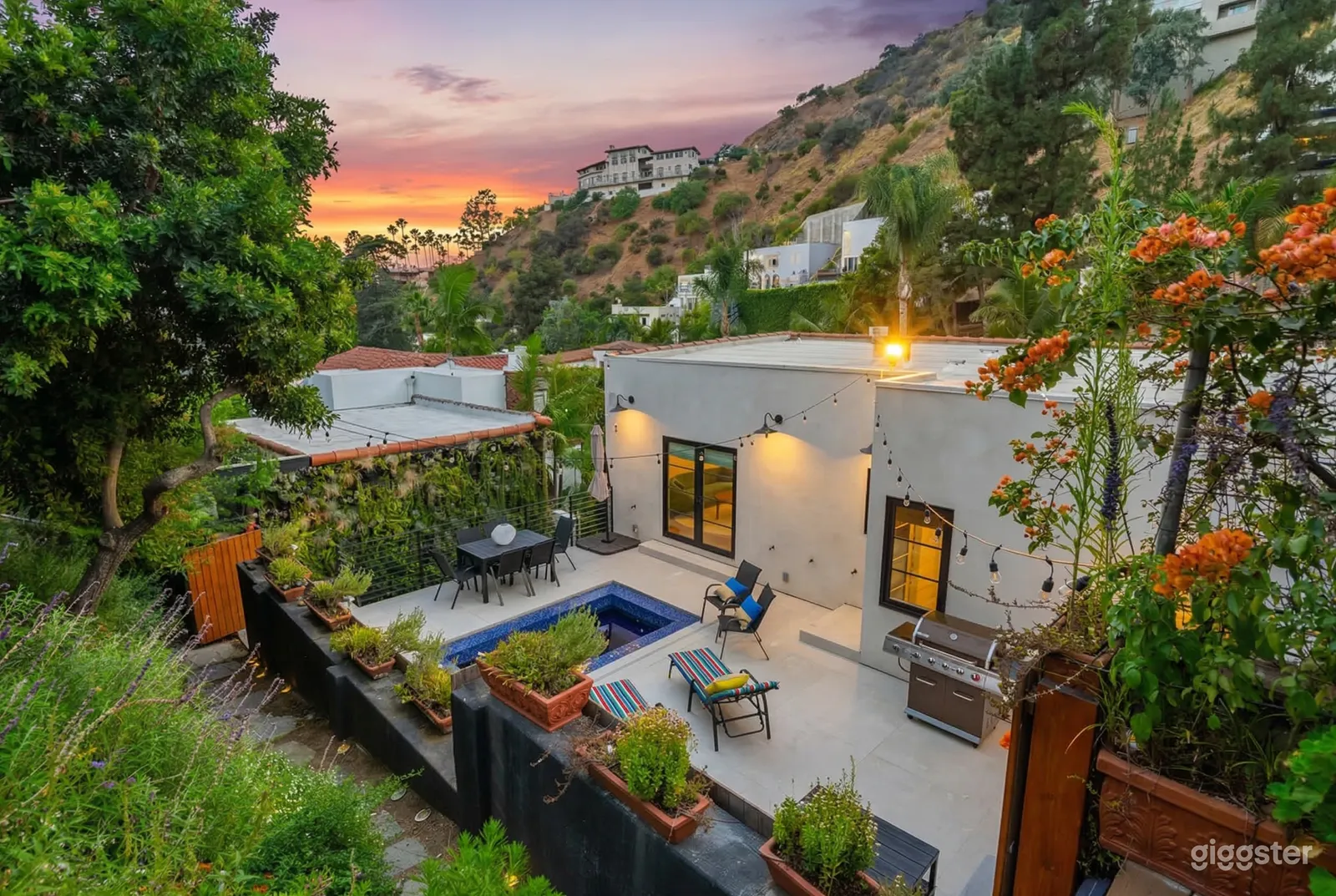 A small swimming pool, dining, and barbecue area in front of a modern flat-roofed home in the mountains.