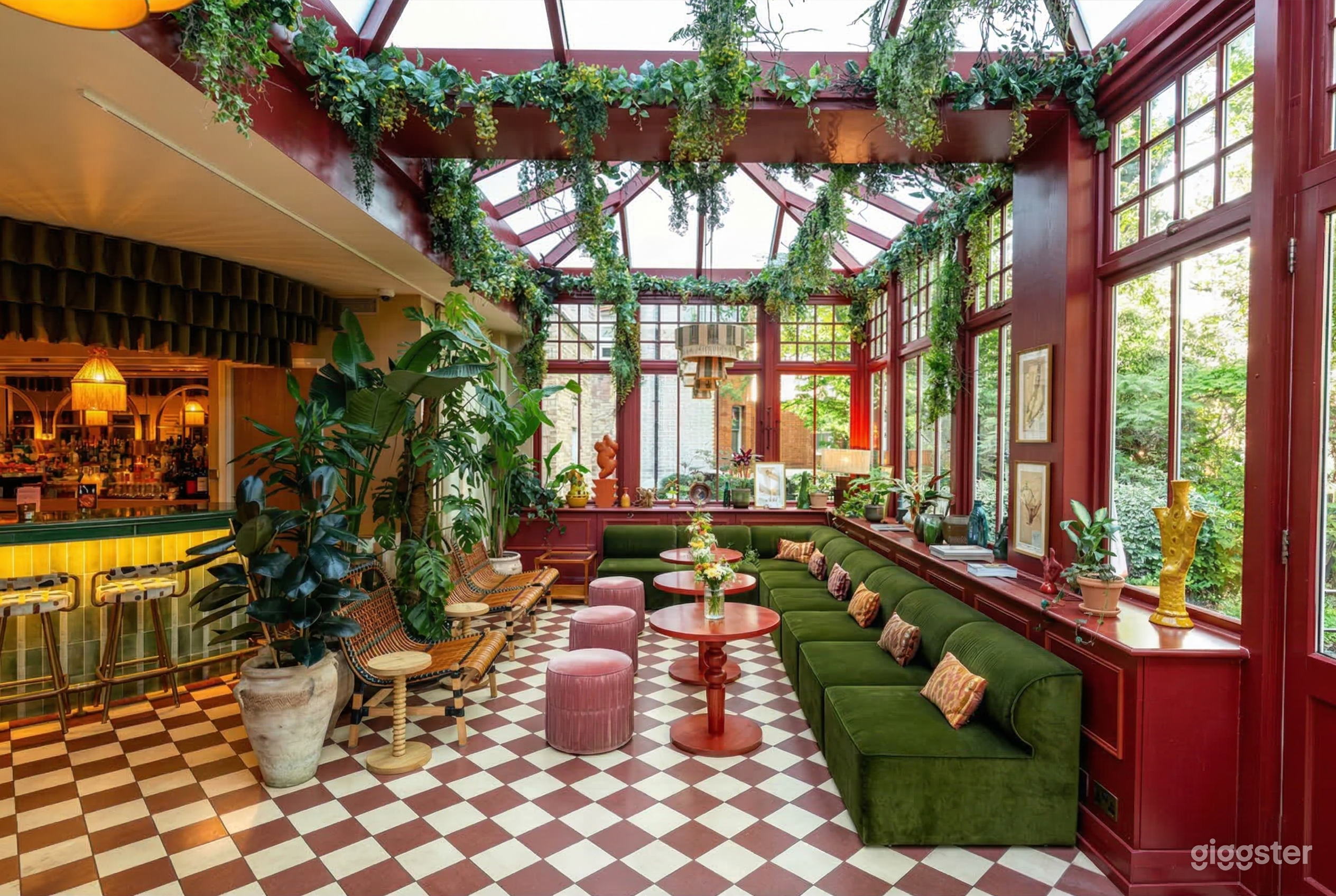Large windows and a glass ceiling decorated with vines surround green benched seating in a pretty brunch restaurant.