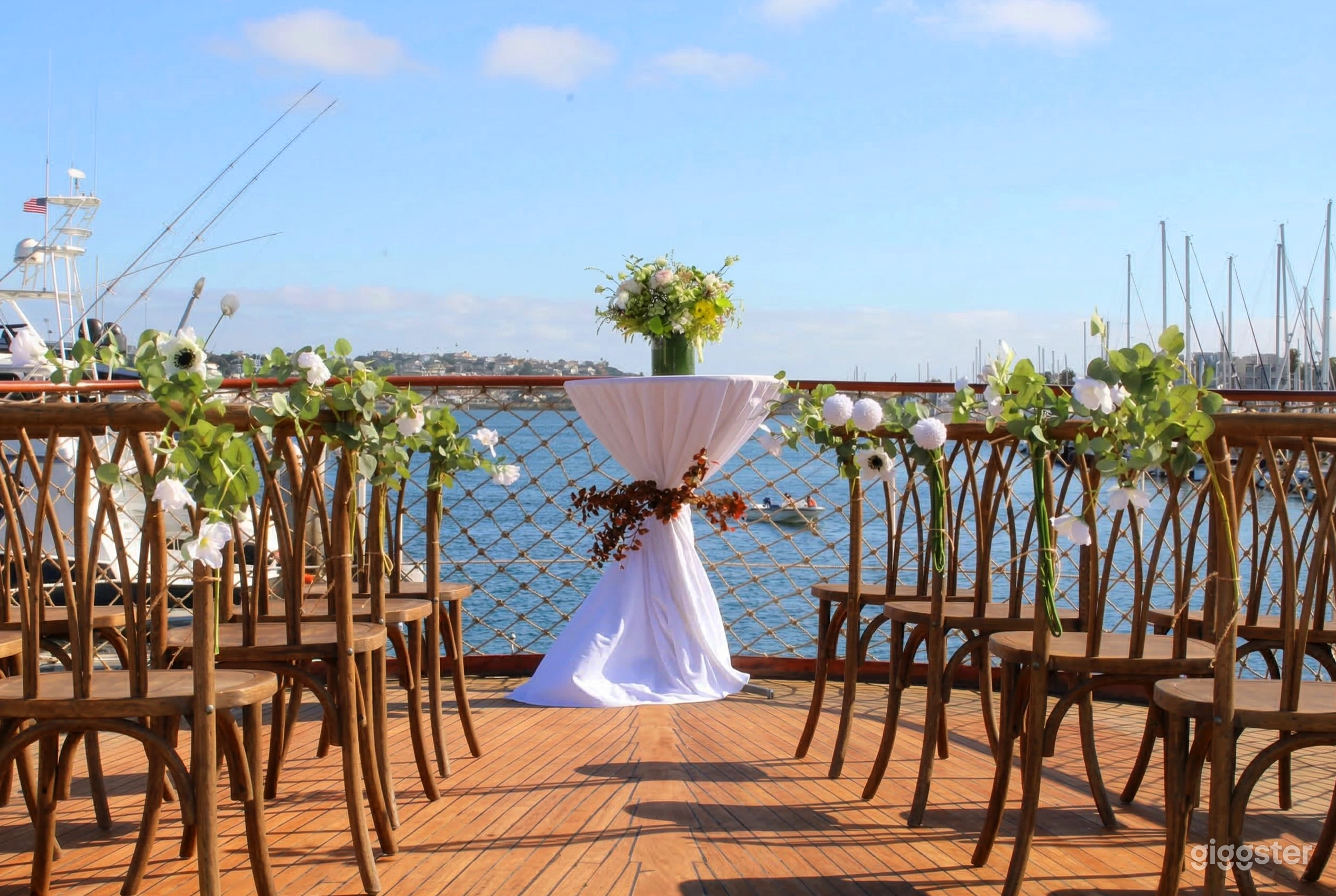 A small white table sits in front of rows of chairs decorated with flowers, and all face a fenced waterfront.