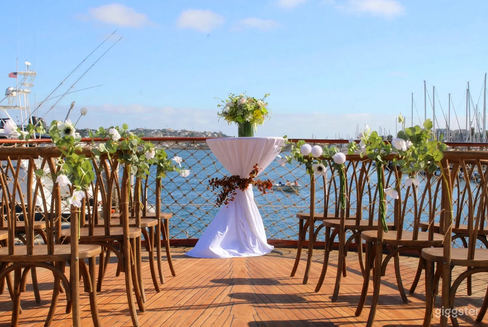 A small white table sits in front of rows of chairs decorated with flowers, and all face a fenced waterfront.