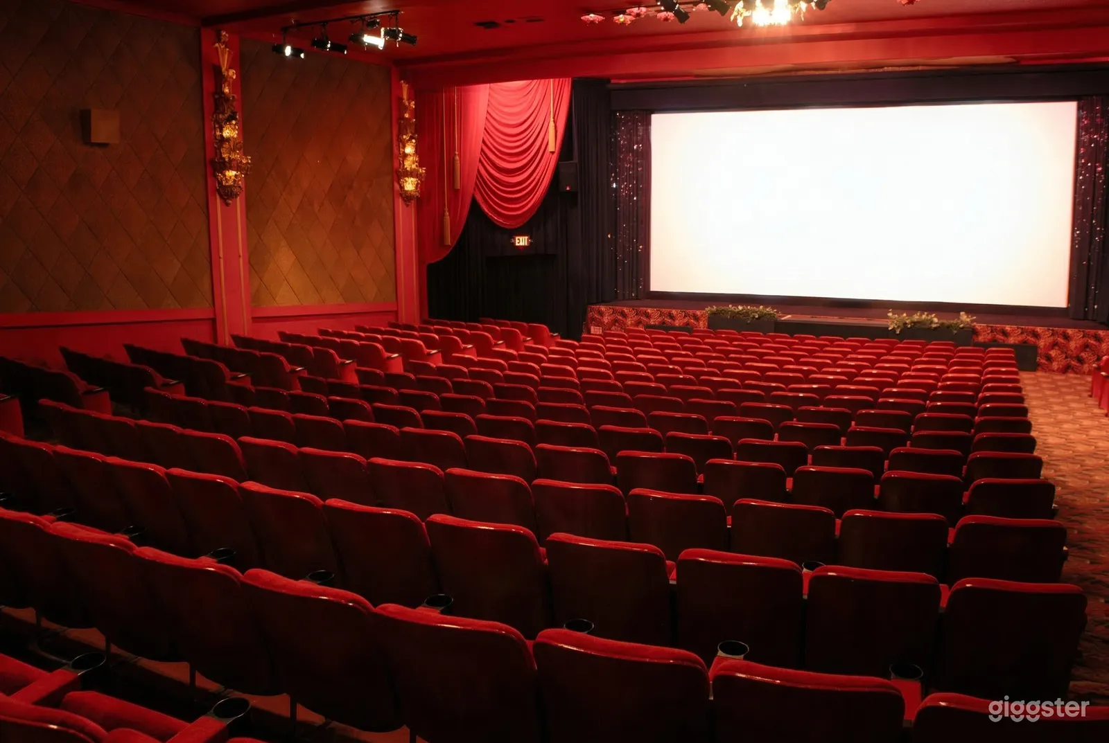 Many rows of red cinema seating faces a white movie screen.