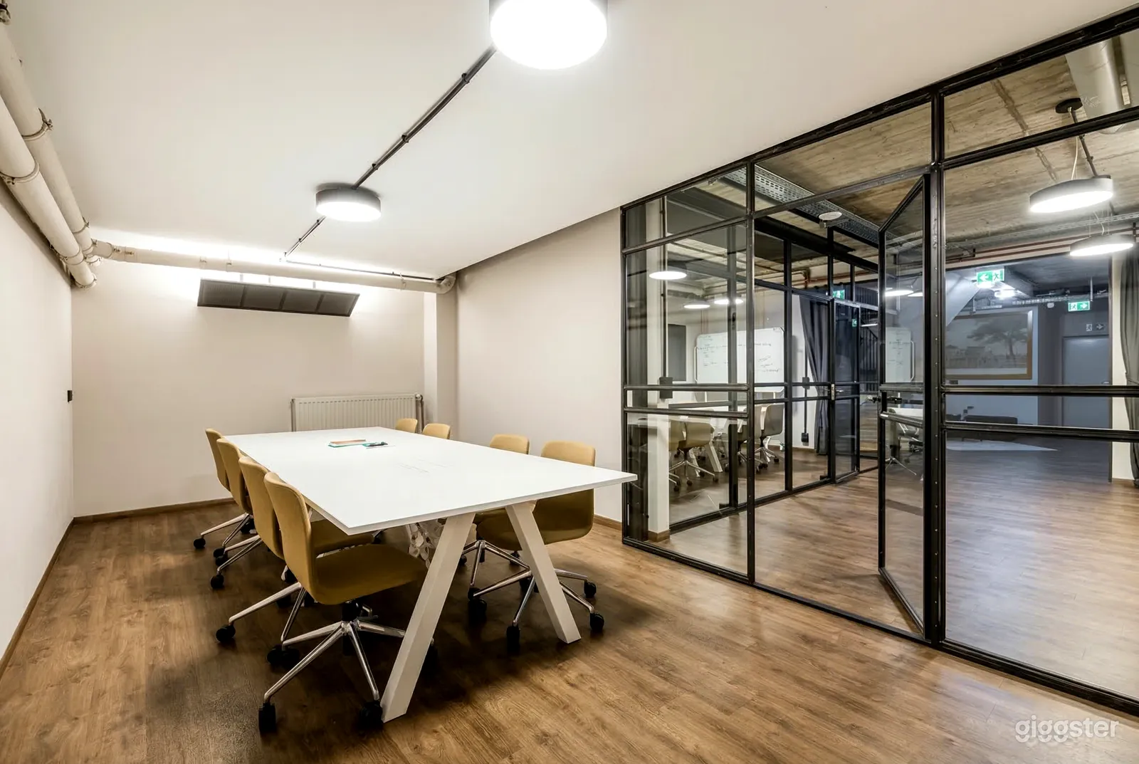 A long white conference table sits in a meeting room with one glass wall and door.
