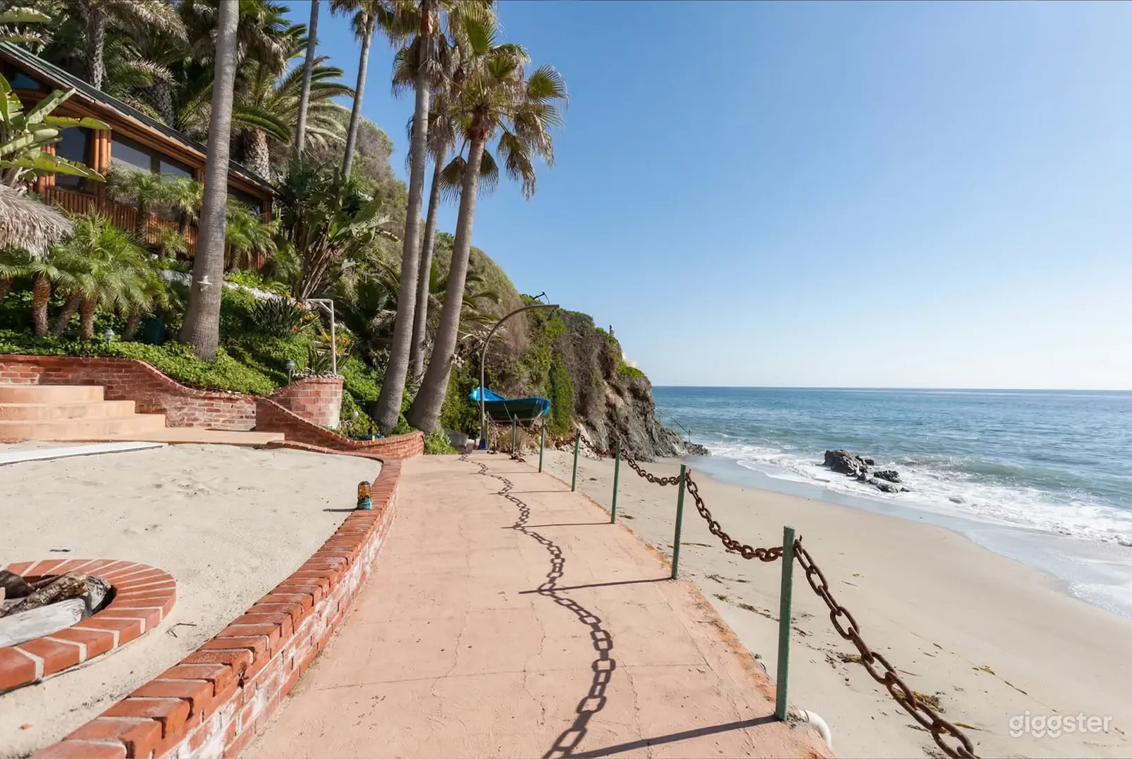 A large cement and brick patio with fencing overlooks a small sandy beach on the ocean.