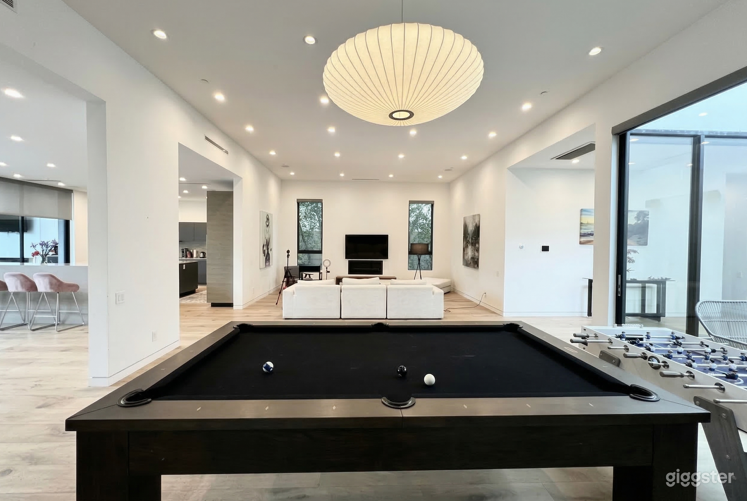 A white walled open concept home has a large games room area against a windowed wall.