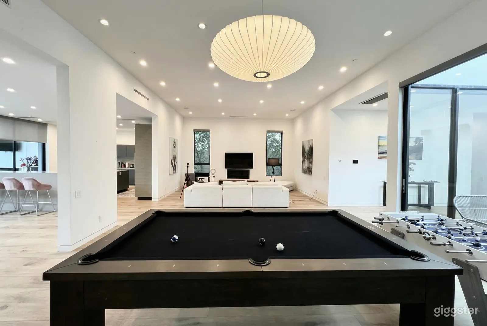 A white walled open concept home has a large games room area against a windowed wall.