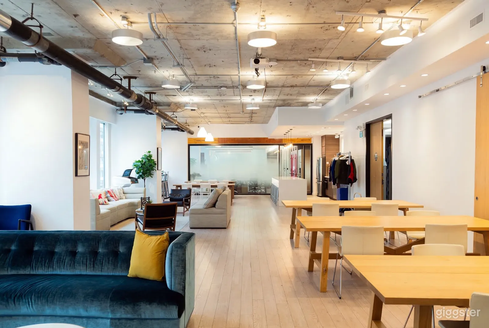 A bright meeting room has an area with couch seating on one side and work tables and chairs on the other.