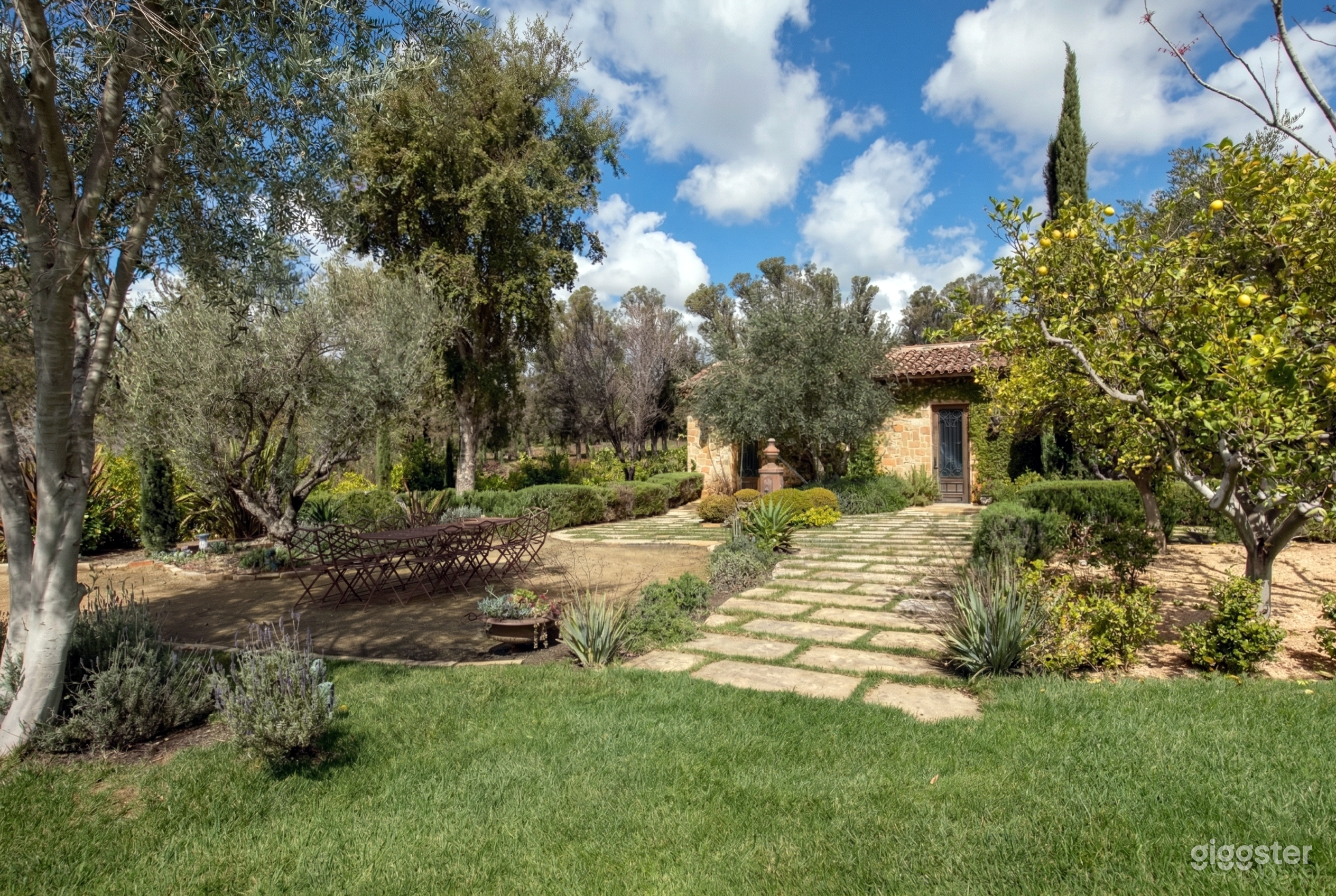 A decorative patio sits amongst a desert style garden behind a stone home.