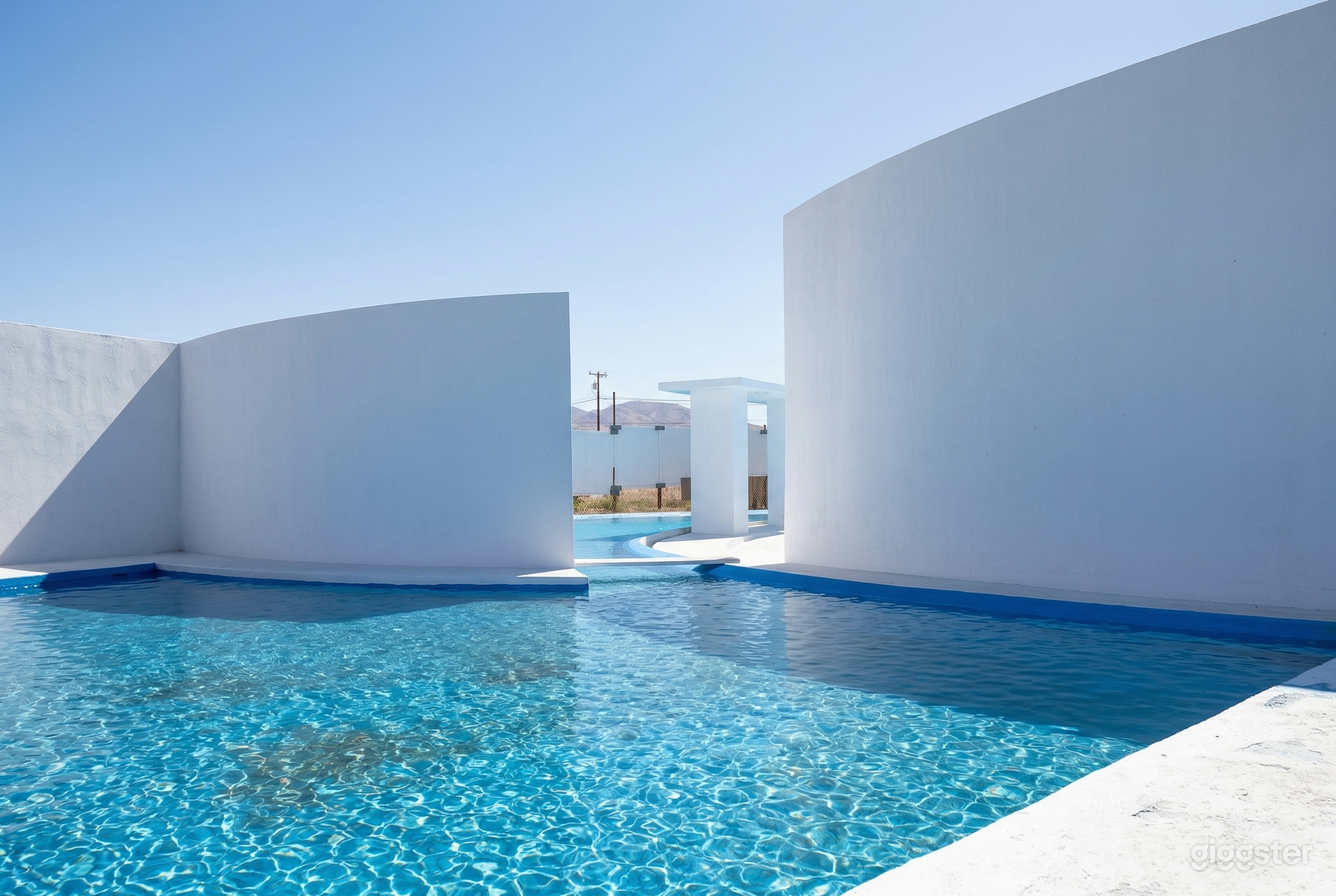 An expansive pool with high white cement decorative walls sits under the open sky.