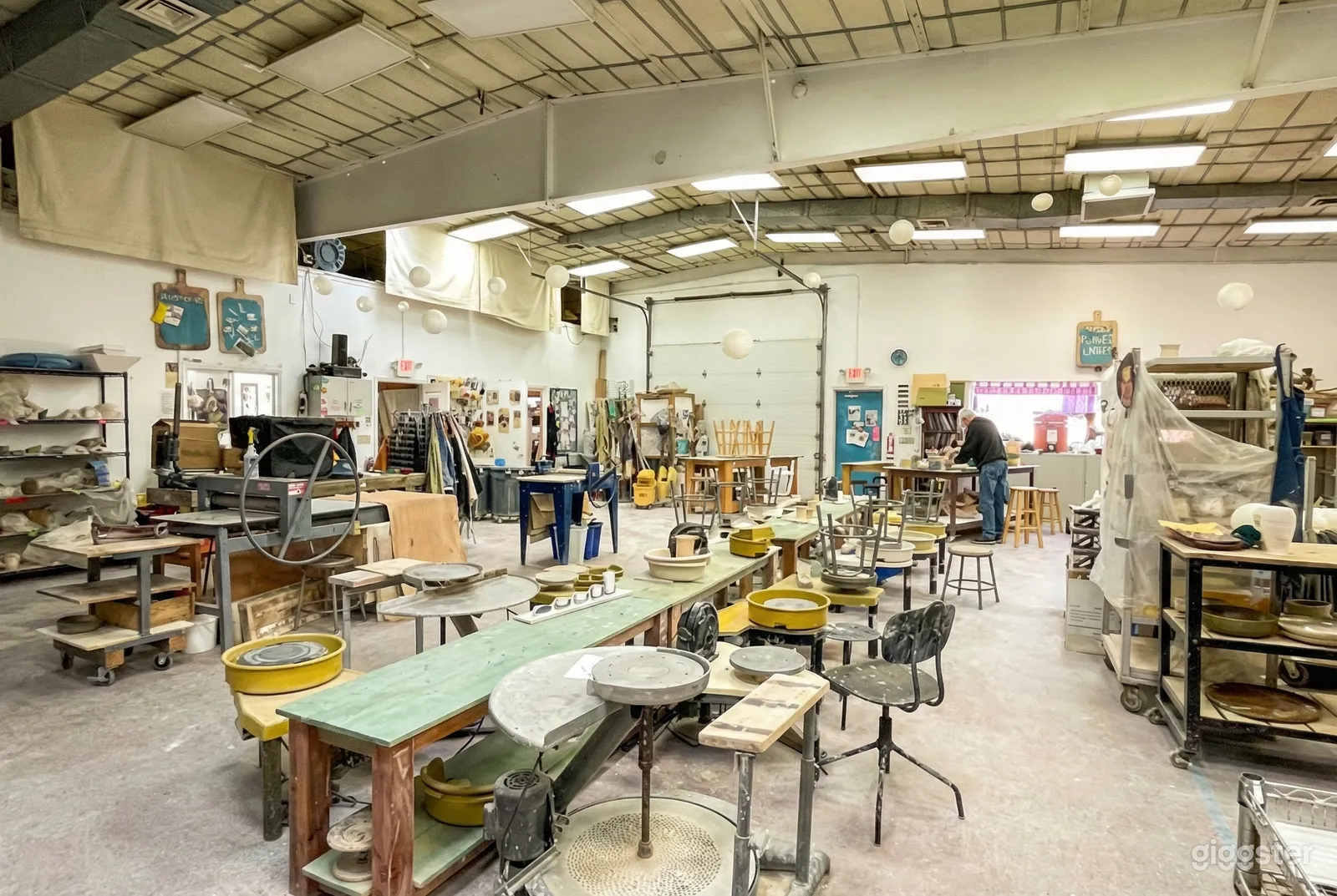 Large  well-lit garage venue with pottery wheels, supplies and stools at long tables.