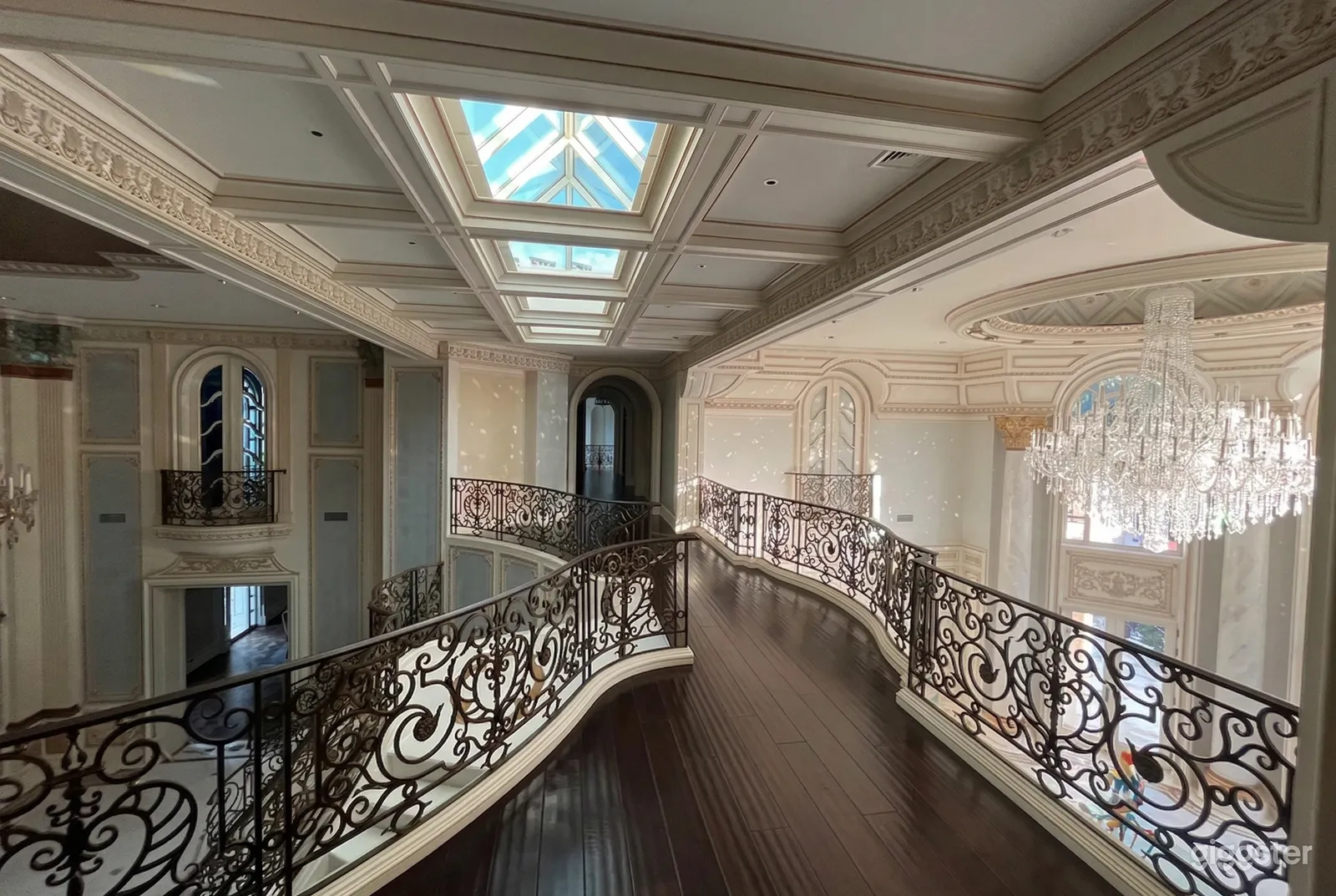 The upper balcony of an event room has wrought iron fencing, and an ornate ceiling with skylights and chandeliers.