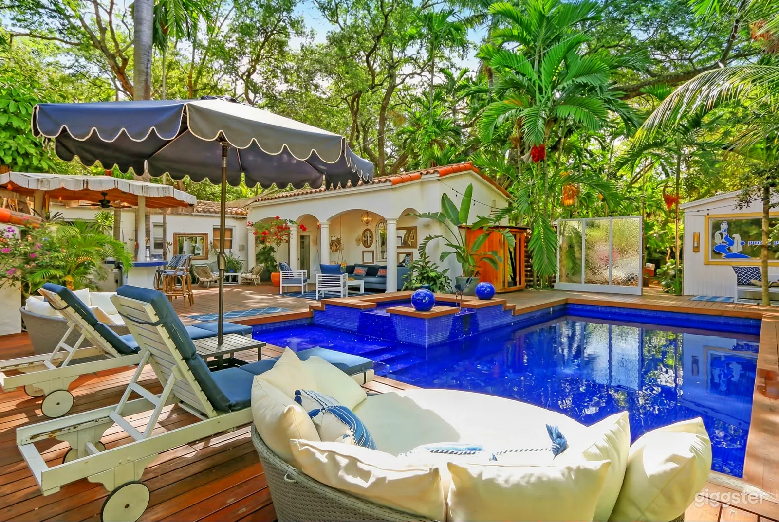A pool lined in deep blue is the focal point of a large wooden deck in front of a Spanish style villa.
