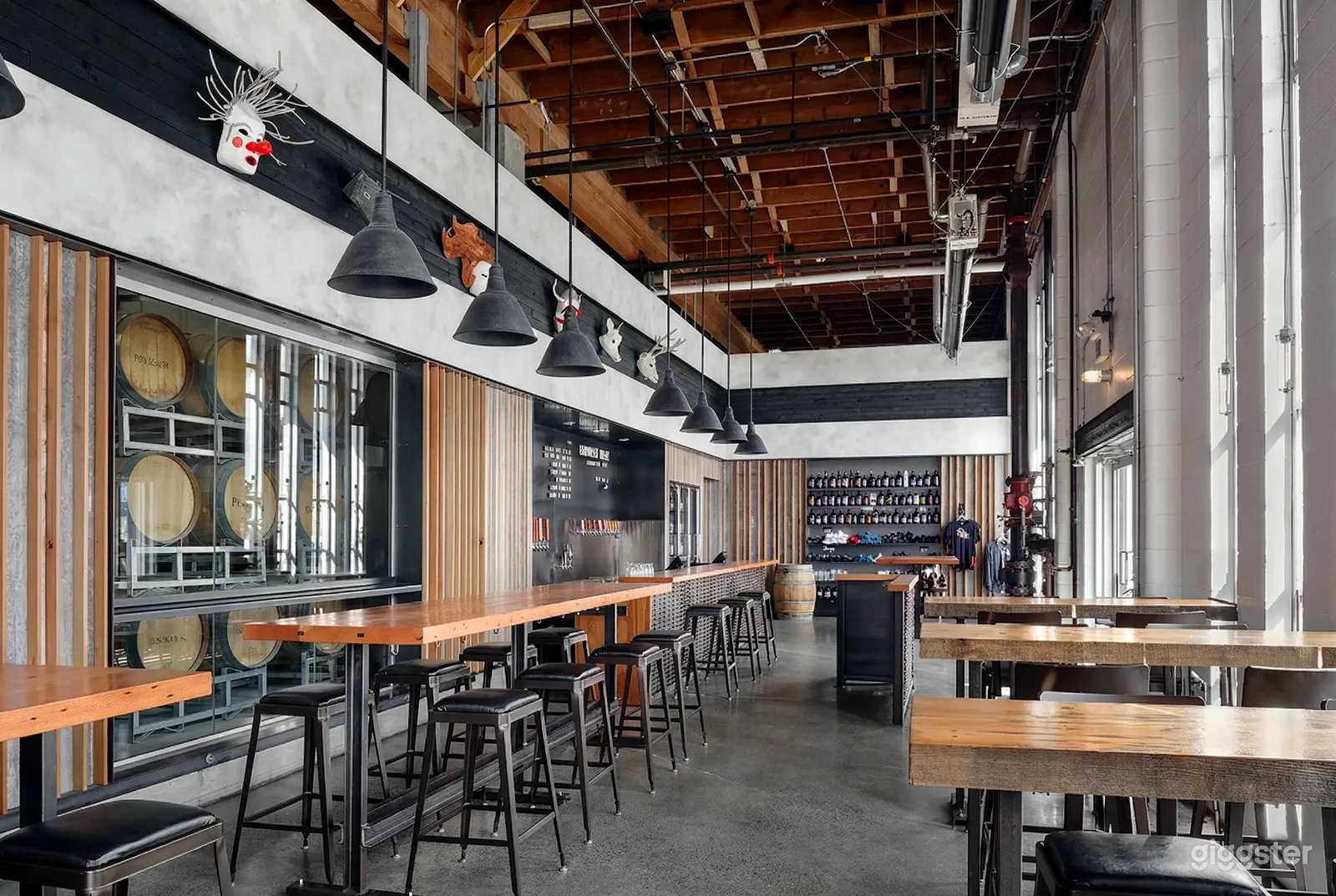 Long benches and stools fill an industrial style brewery with visible pipes and low black lighting.