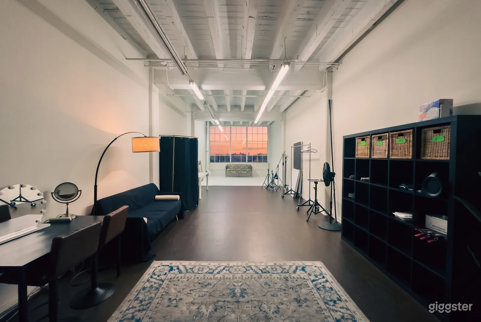 A industrial style room is empty in the middle with a couch, shelving, and props on the outer walls.