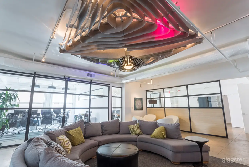 A semi circular couch sits in a space with ultra modern lighting overhead, with a conference room behind a glass wall.