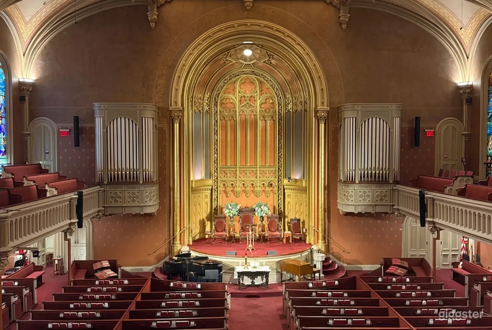 An ornate stage with gold detailing sits at the front of a cathedral style chapel, with balconies on either side of the room.