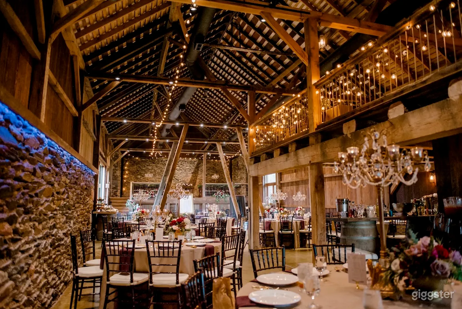 A ranch style room is filled with tables and black chairs and is decorated with string lights and chandeliers.
