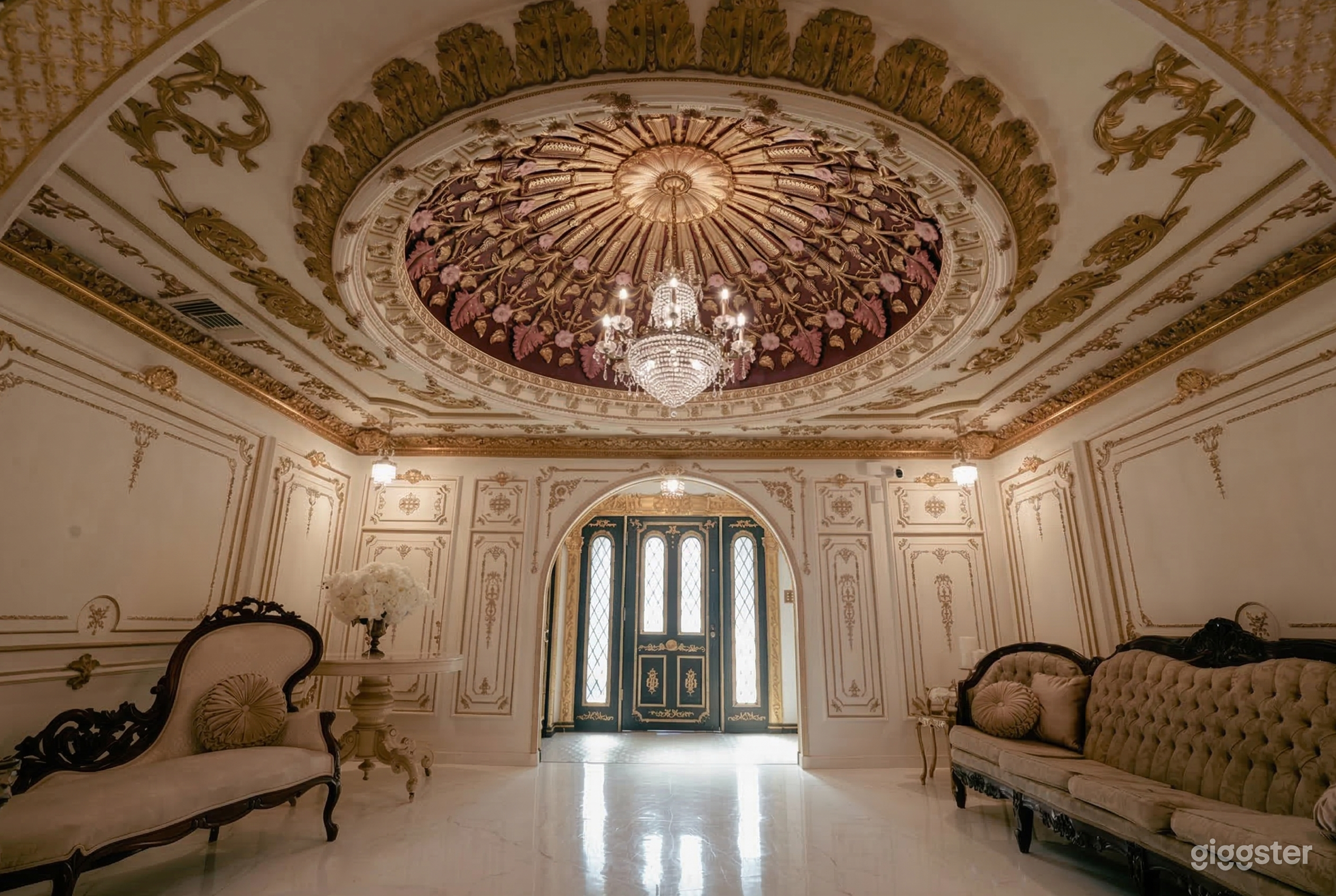 A ballroom style room has an ornate gold and beige ceiling over a period chaise lounge and couch.