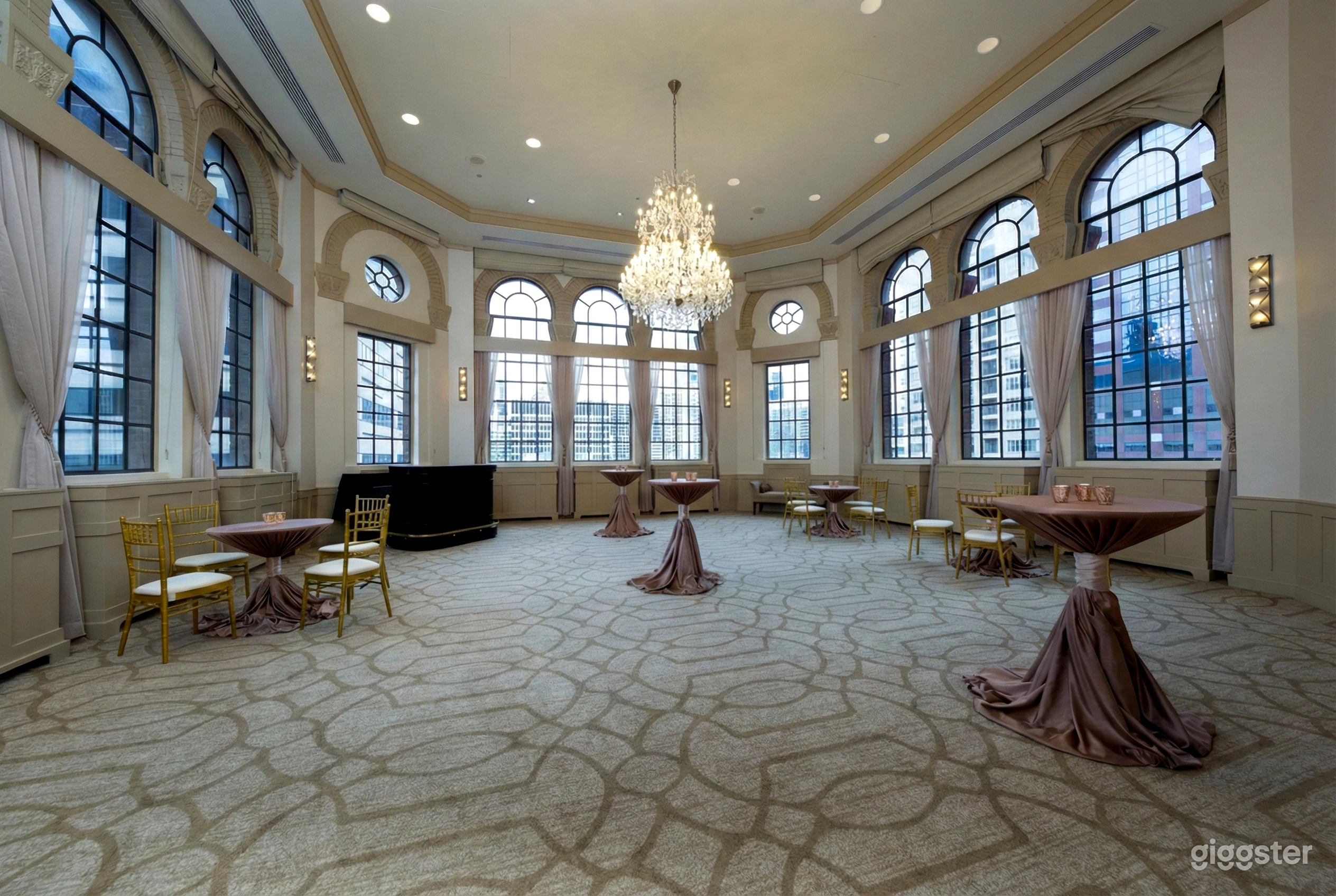 Decorative tables are highlighted by a chandelier in a window-filled room set to host a prom.