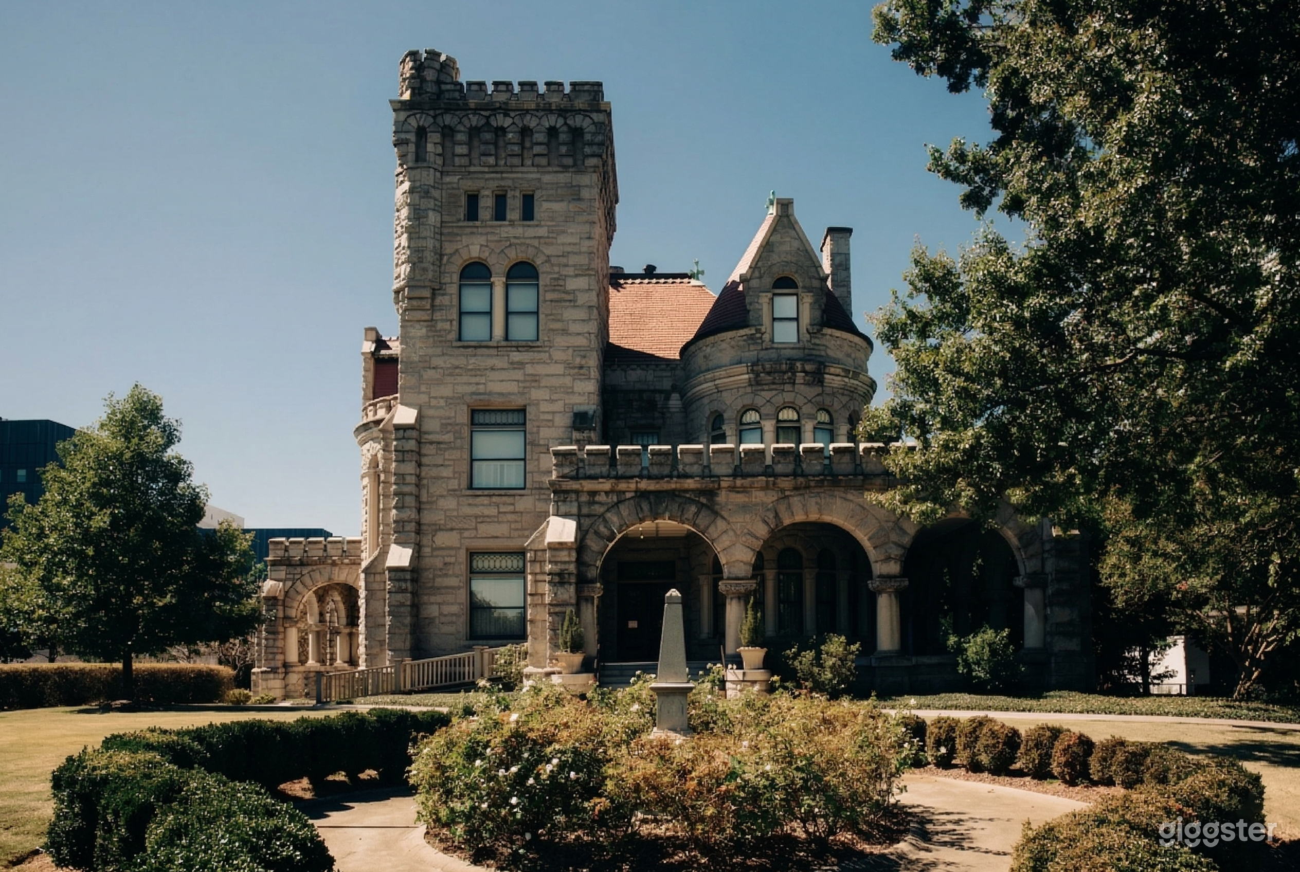 A castle style home with a turret and tower faces a round hedged garden