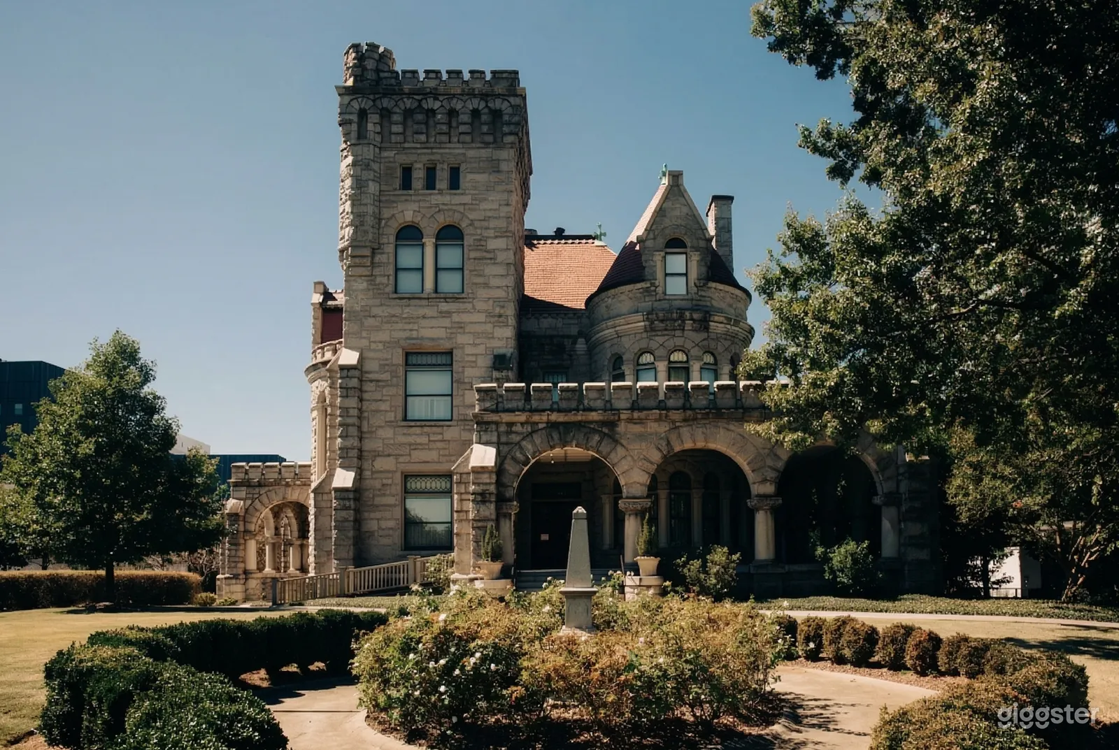 A castle style home with a turret and tower faces a round hedged garden