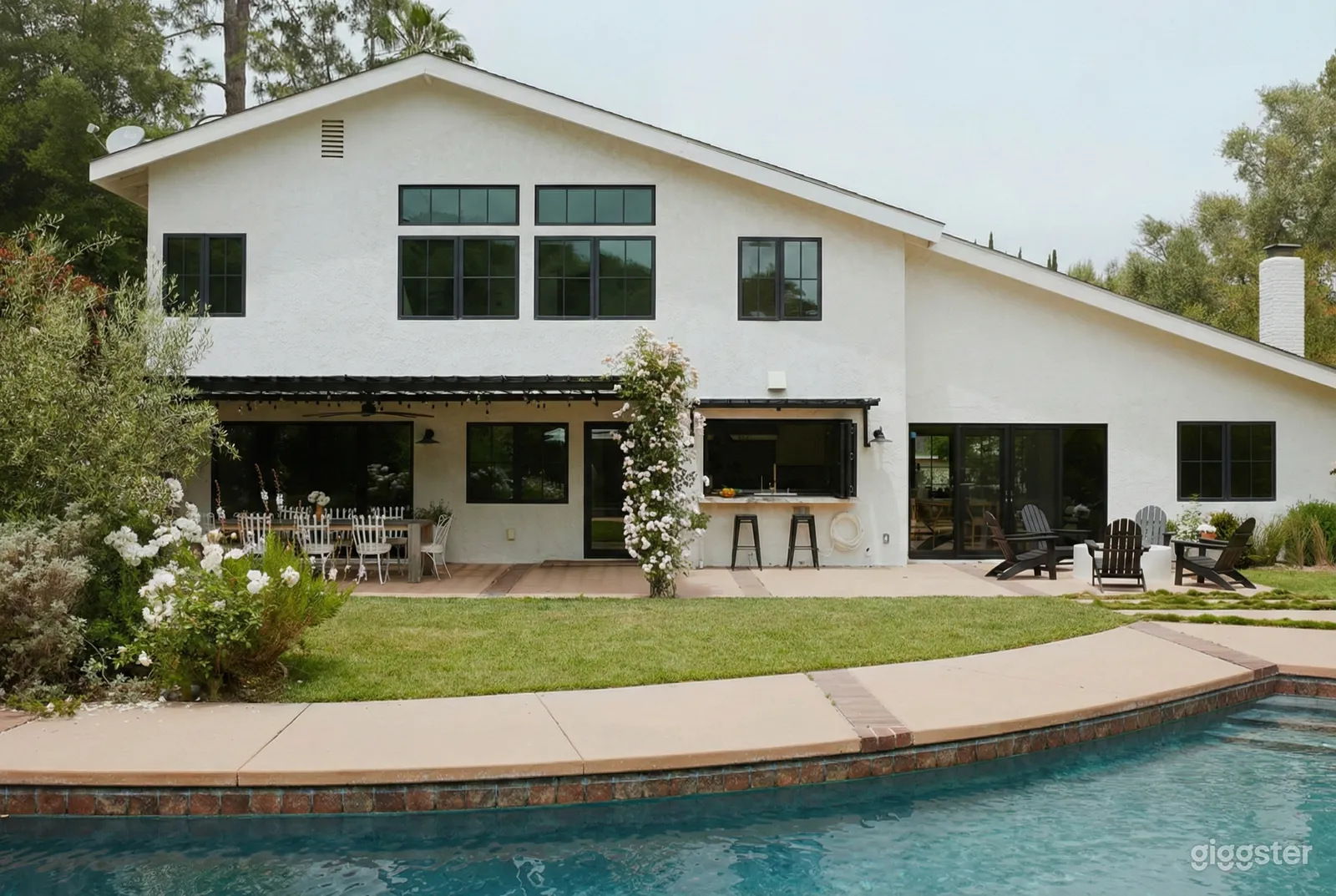 White modern home with a garden area, seating and a pool in front.