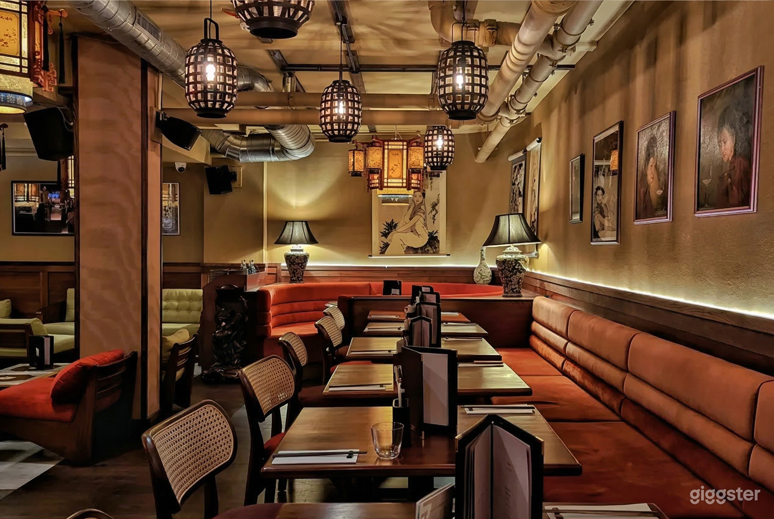 A restaurant with orange benches and wicker seating, with industrial-style pipes and black cage-lamps as ceiling decor.