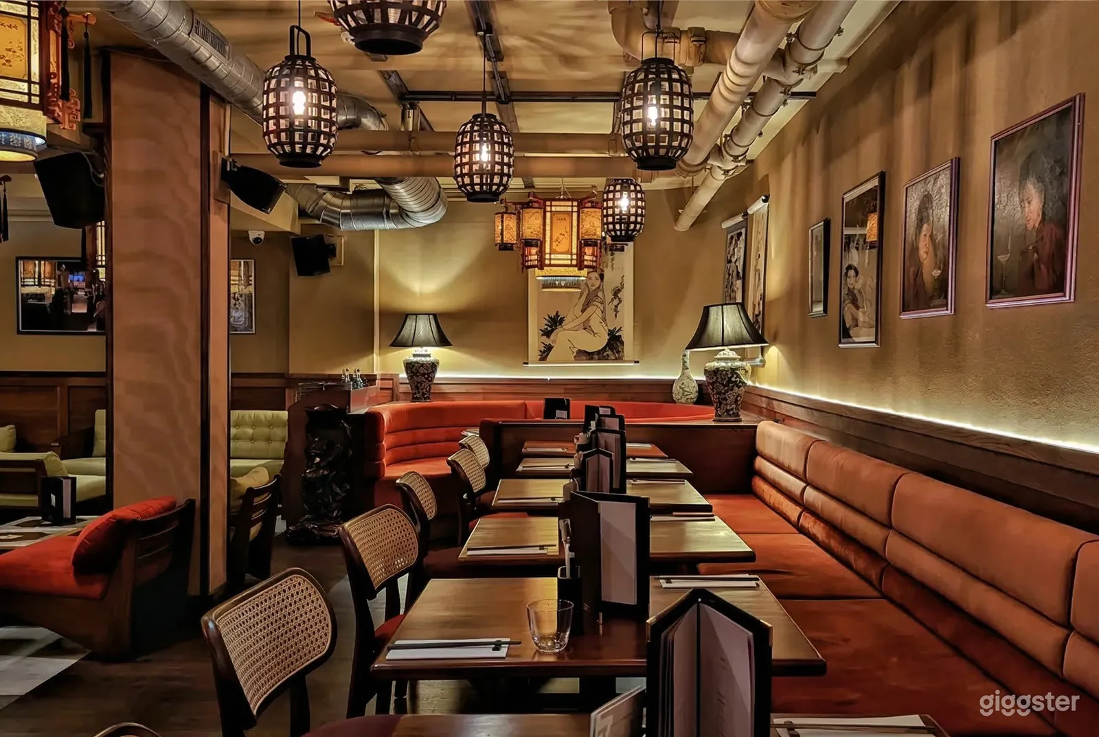 A restaurant with orange benches and wicker seating, with industrial-style pipes and black cage-lamps as ceiling decor.
