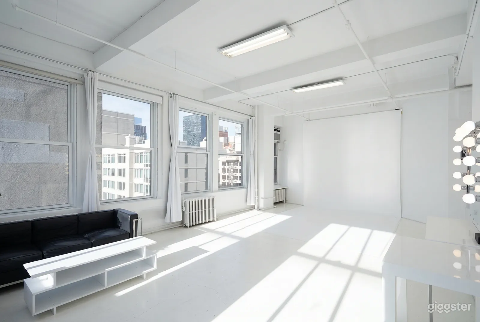 An open, studio type room is styled with a white screen, white curtains and white walls.